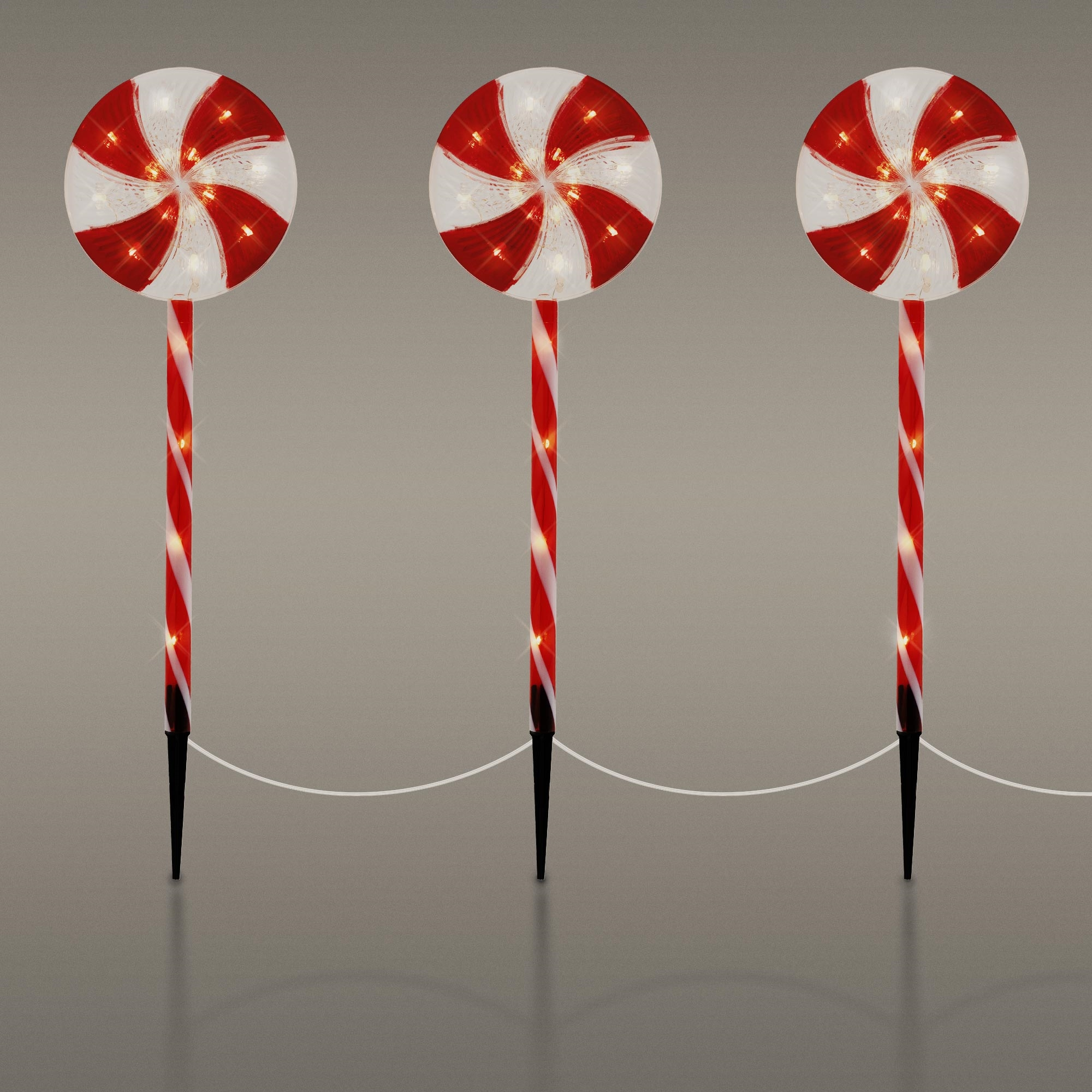 Drei beleuchtete Rasenornamente in Form von Zuckerstangen. Rote und weiße Spiralstangen mit leuchtenden roten und weißen Spitzen. Erdspieße.