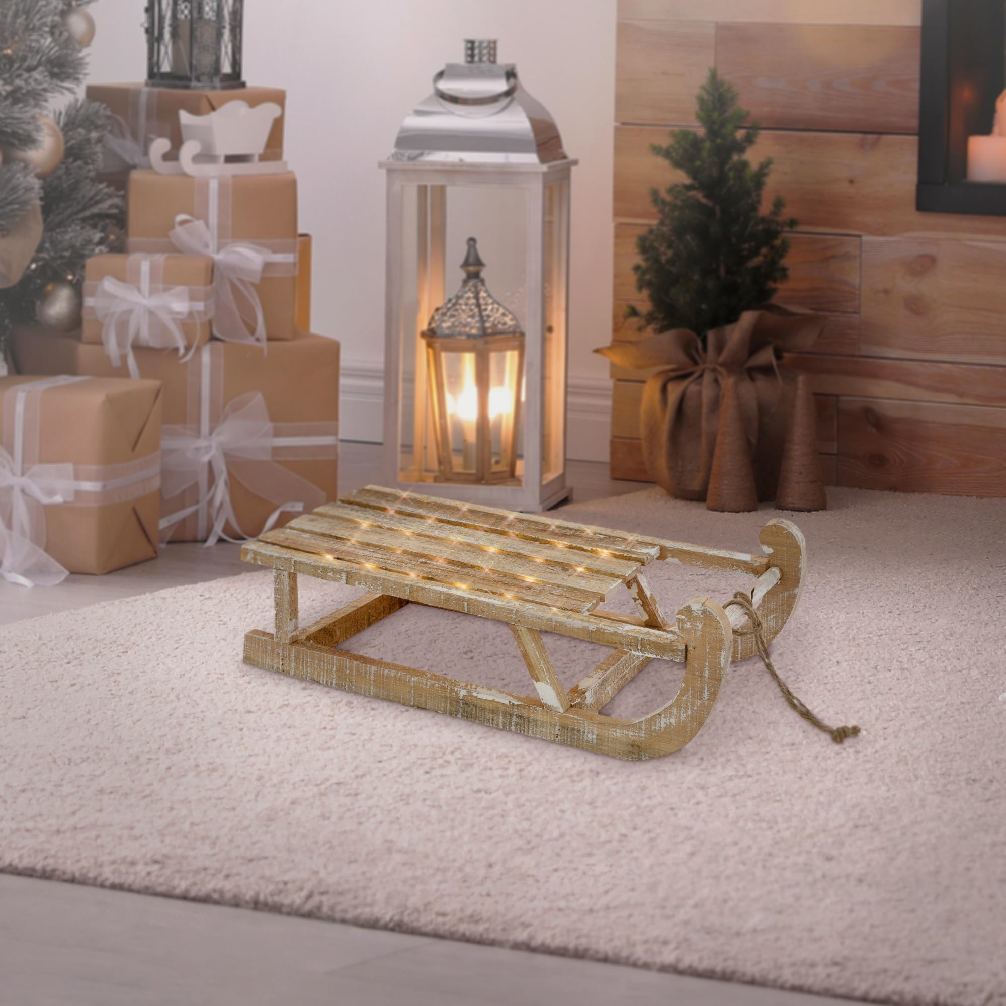 Ein Holzschlitten mit Lichtern liegt auf einem Teppich. Geschenke und ein Weihnachtsbaum sind im Hintergrund.