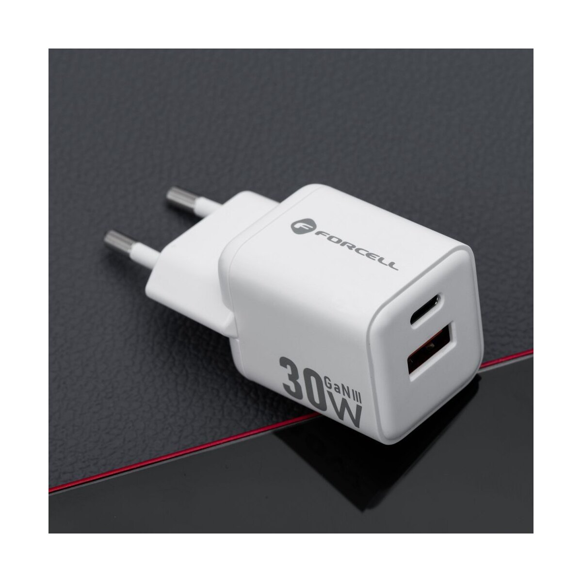 Un caricatore bianco Forcell 30W con porta USB-C e USB è appoggiato su una superficie scura. Il caricatore è collegato.