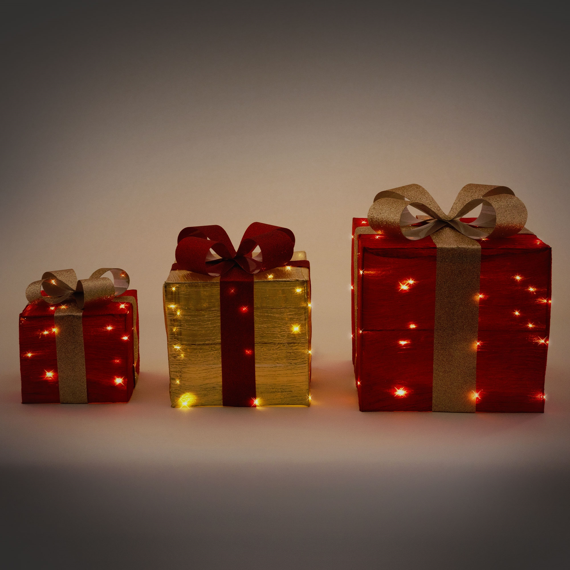 Drei beleuchtete Geschenkboxen. Rot, Gold und Rot. Goldene Schleifen. Mit kleinen Lichtern beleuchtet.