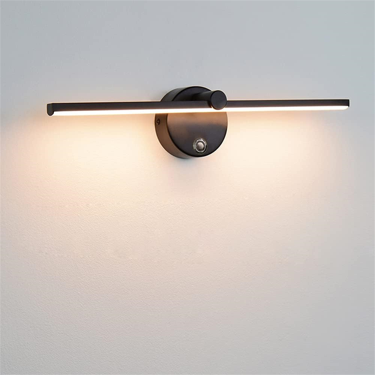 Eine moderne schwarze Wandleuchte mit horizontalem Lichtbalken und rundem Sockel, an einer weißen Wand befestigt.