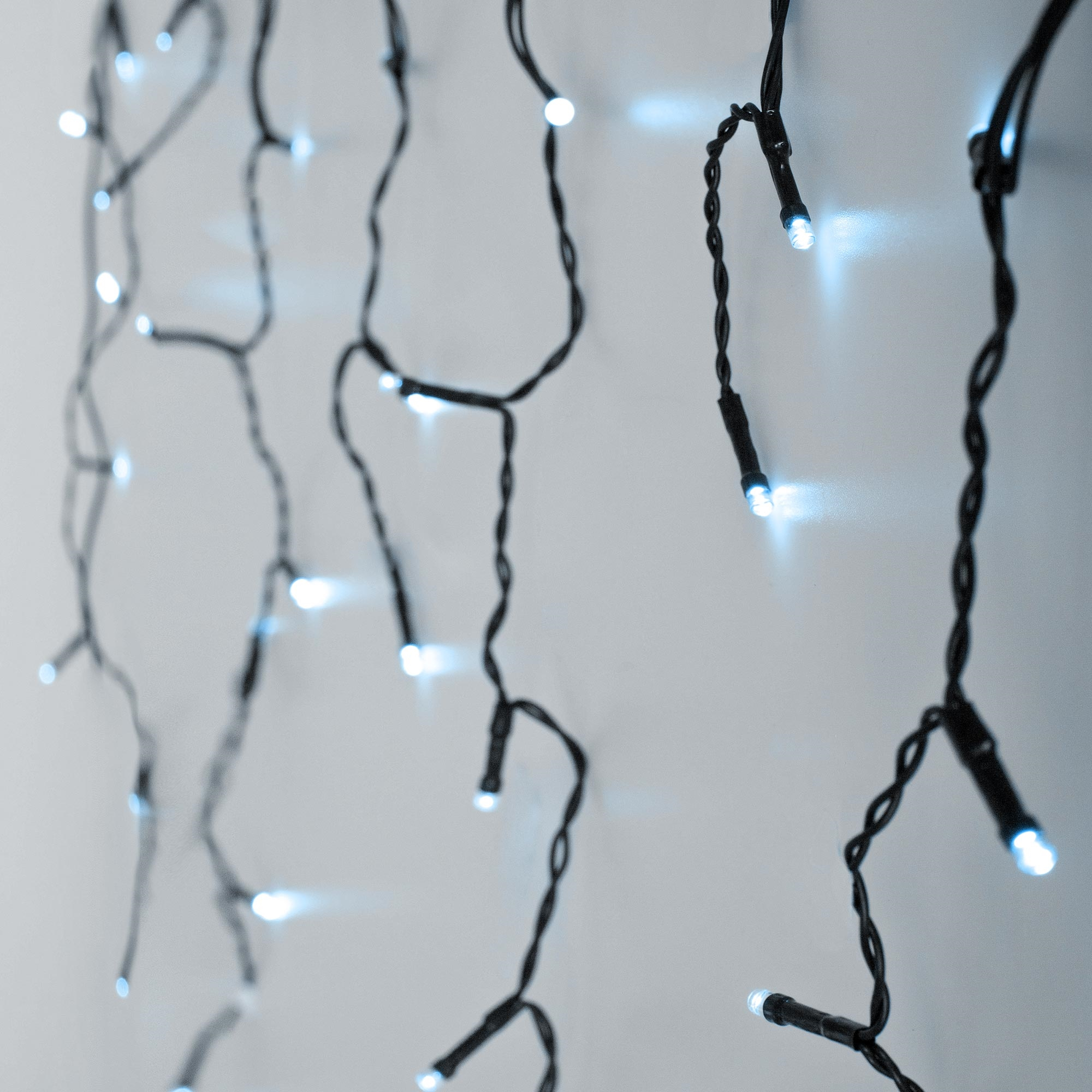 Nahaufnahme von Lichterketten mit kleinen, hellen, weißen LEDs auf schwarzen Drähten vor weißem Hintergrund.