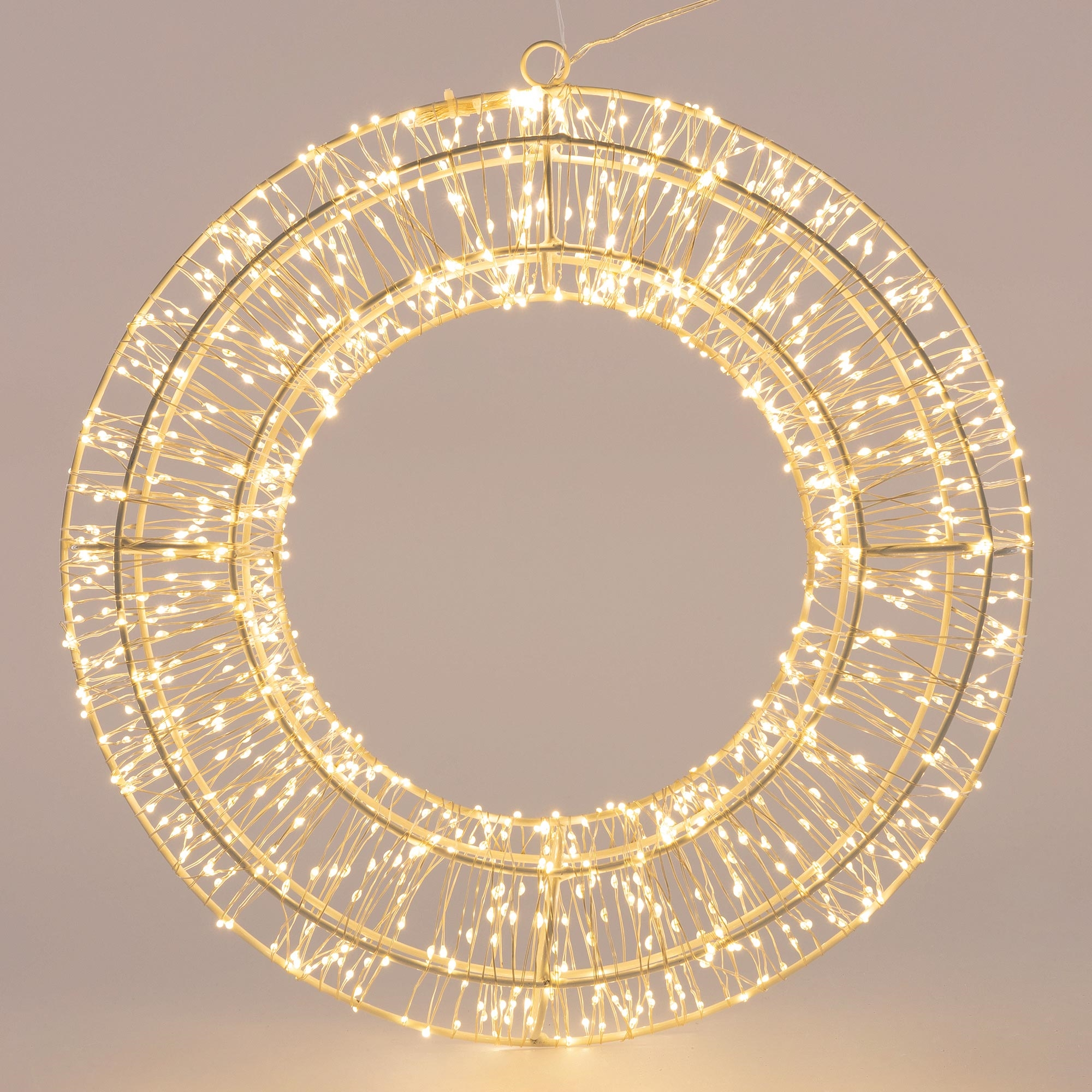 Eine kreisförmige Weihnachtsdekoration mit warmweißen Lichtern, die vor einem neutralen Hintergrund hängt.