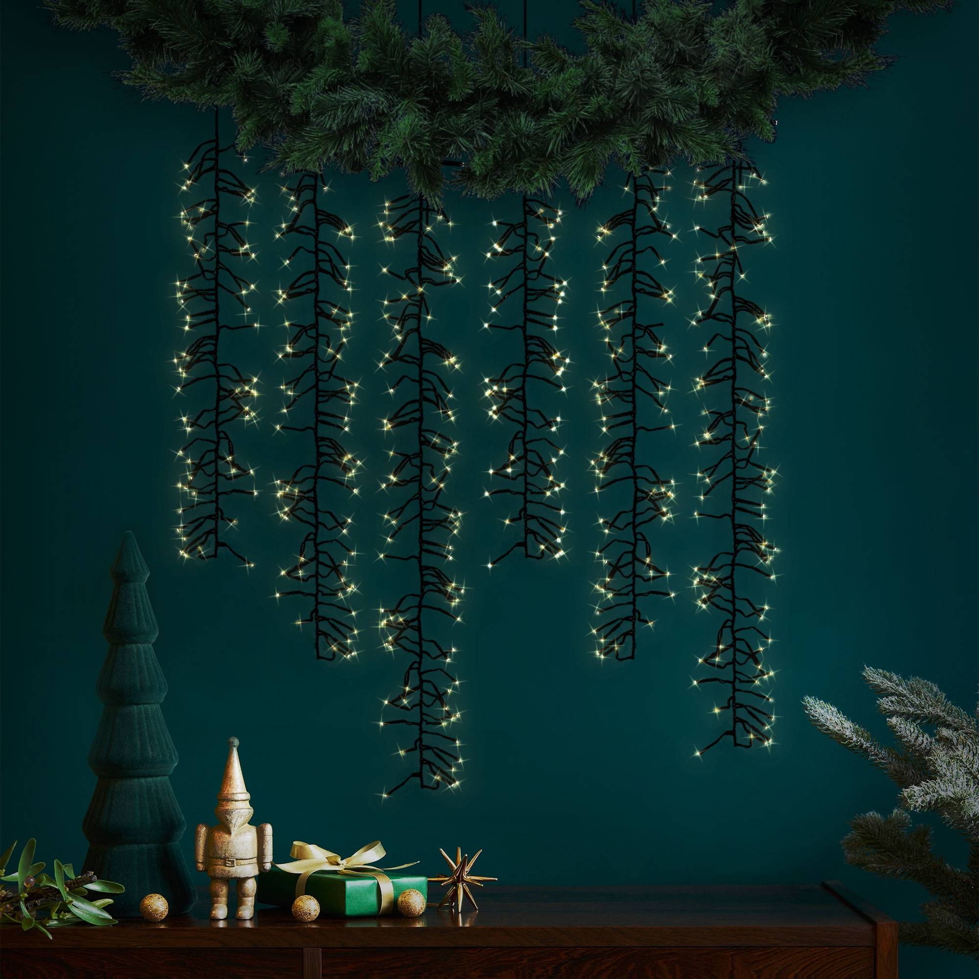 Festliche Szene mit Weihnachtsbeleuchtung, Ornamenten und Dekoration auf dunkler Holzoberfläche vor grüner Wand.