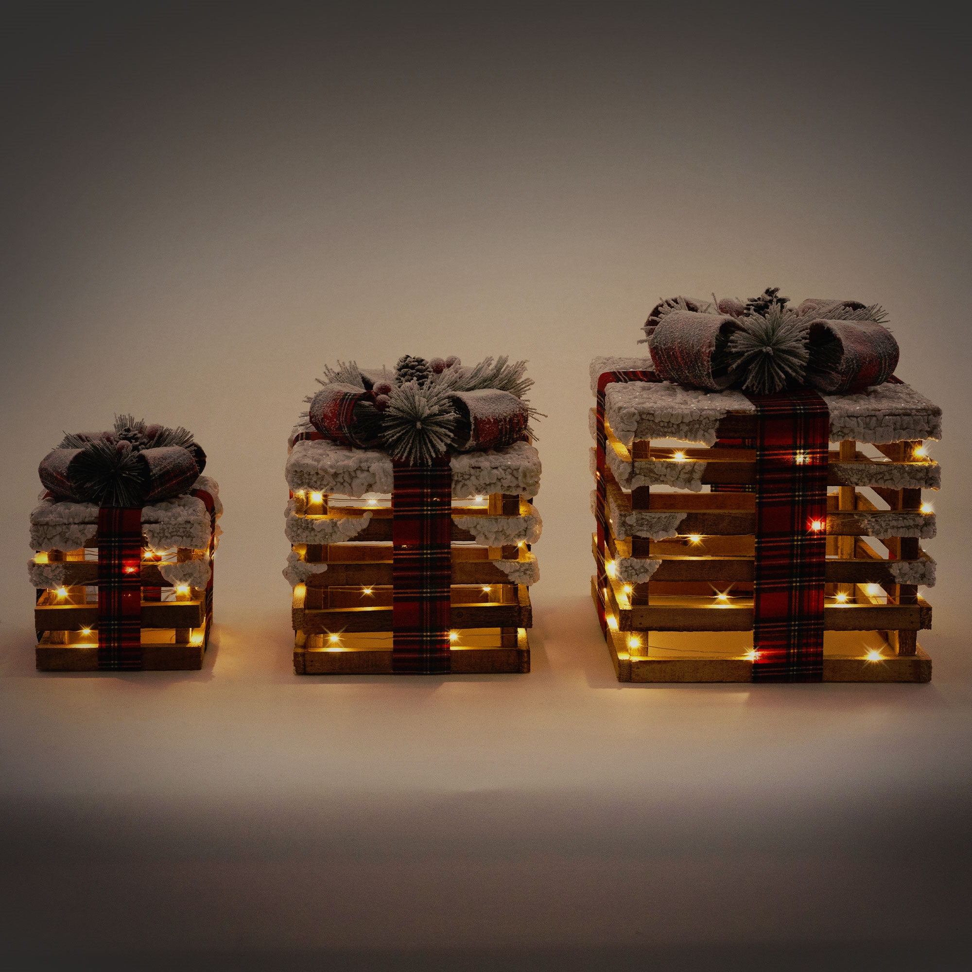 Drei beleuchtete Geschenkboxen. Holzrahmen mit karierten Bändern und Schneeakzenten. Warme Lichter scheinen aus den Boxen.