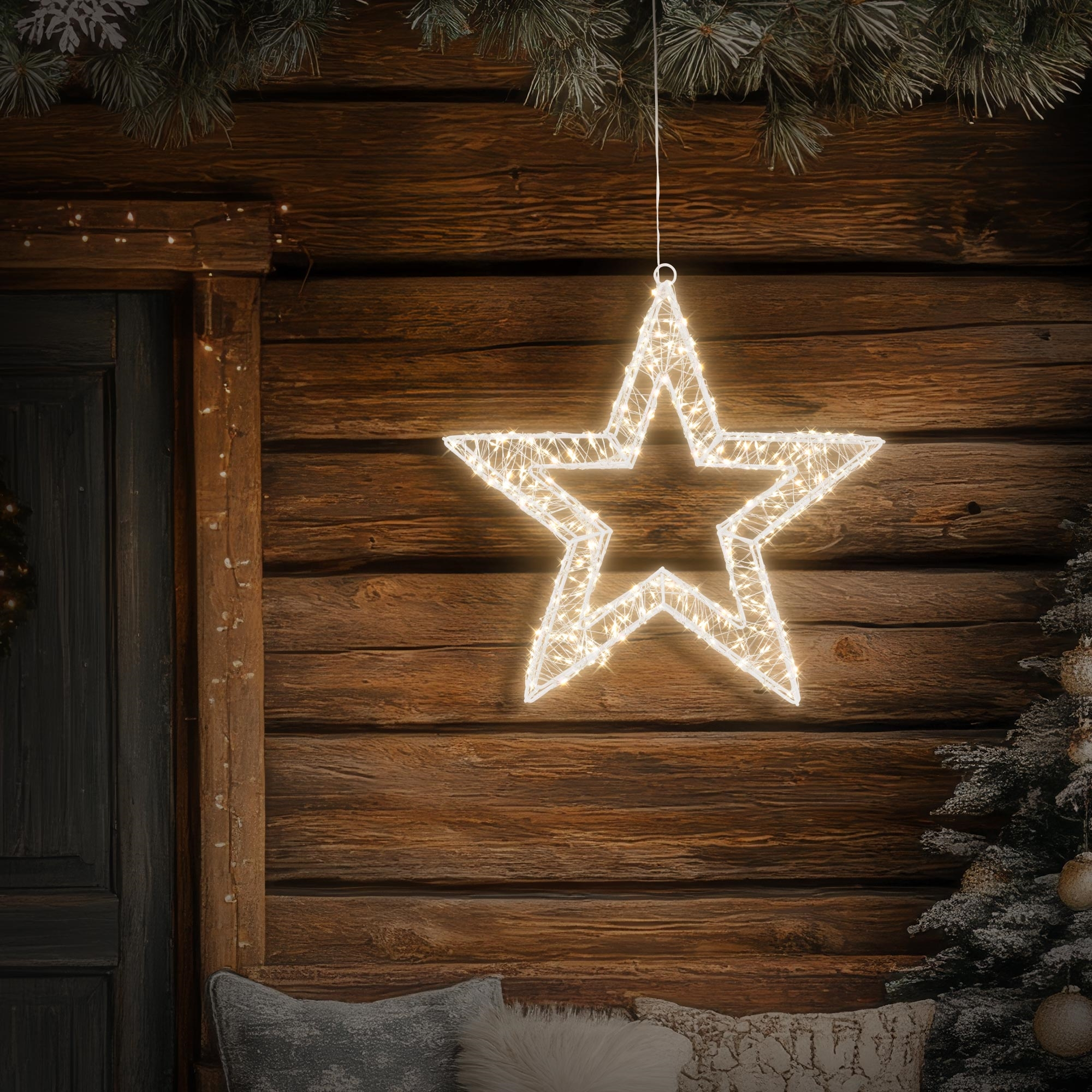 Eine leuchtende Stern-Dekoration hängt vor einer Holzwand. Ein Weihnachtsbaum und eine Tür sind ebenfalls zu sehen.