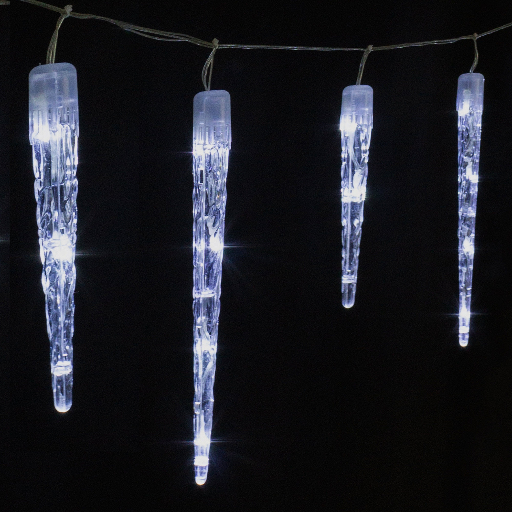 Vier beleuchtete Eiszapfen-Lichter hängen vor schwarzem Hintergrund. Jeder Eiszapfen ist klar mit weißen Lichtern.