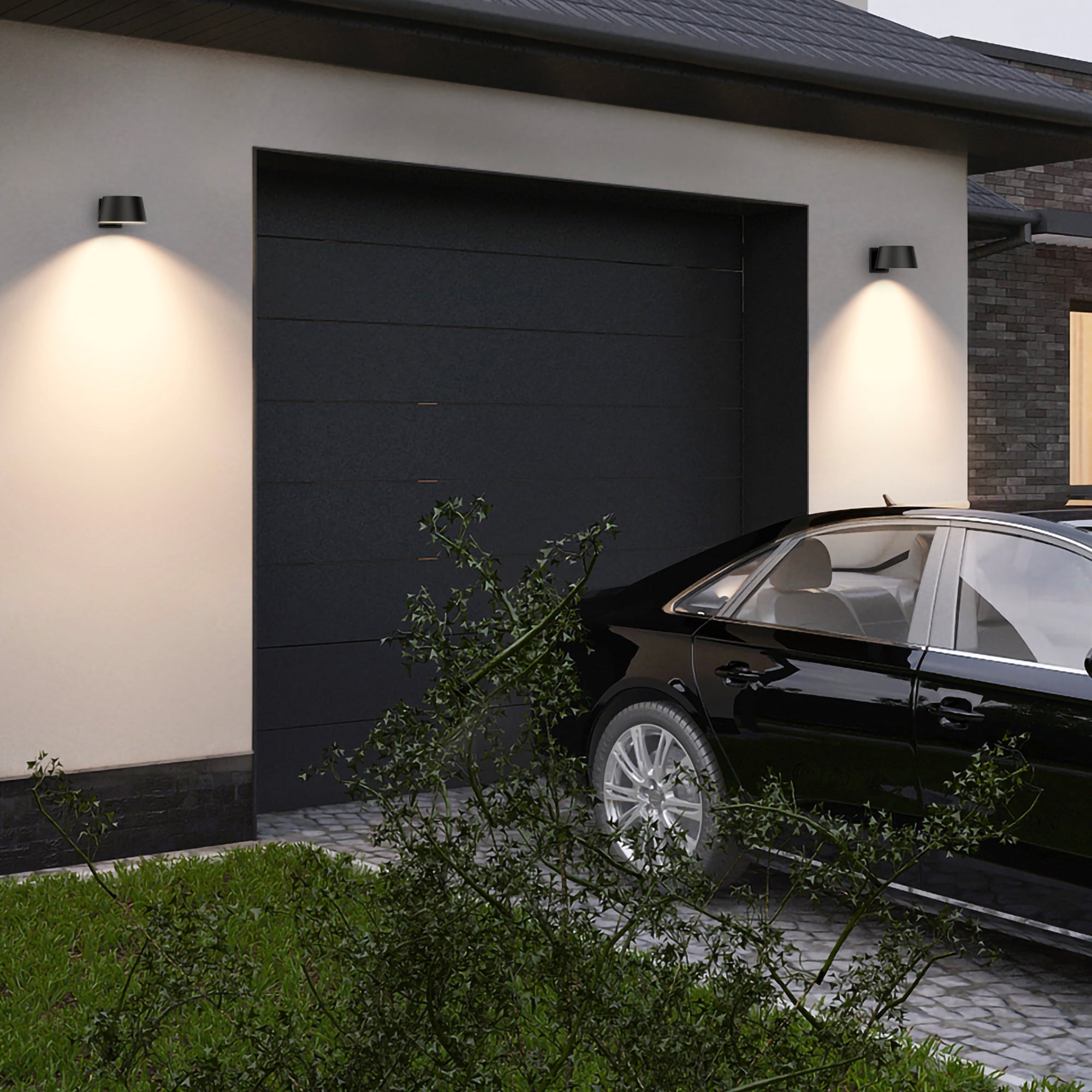 Schwarzes Auto vor einer Garage geparkt. Zwei Lichter beleuchten die Wand. Grüne Büsche im Vordergrund.