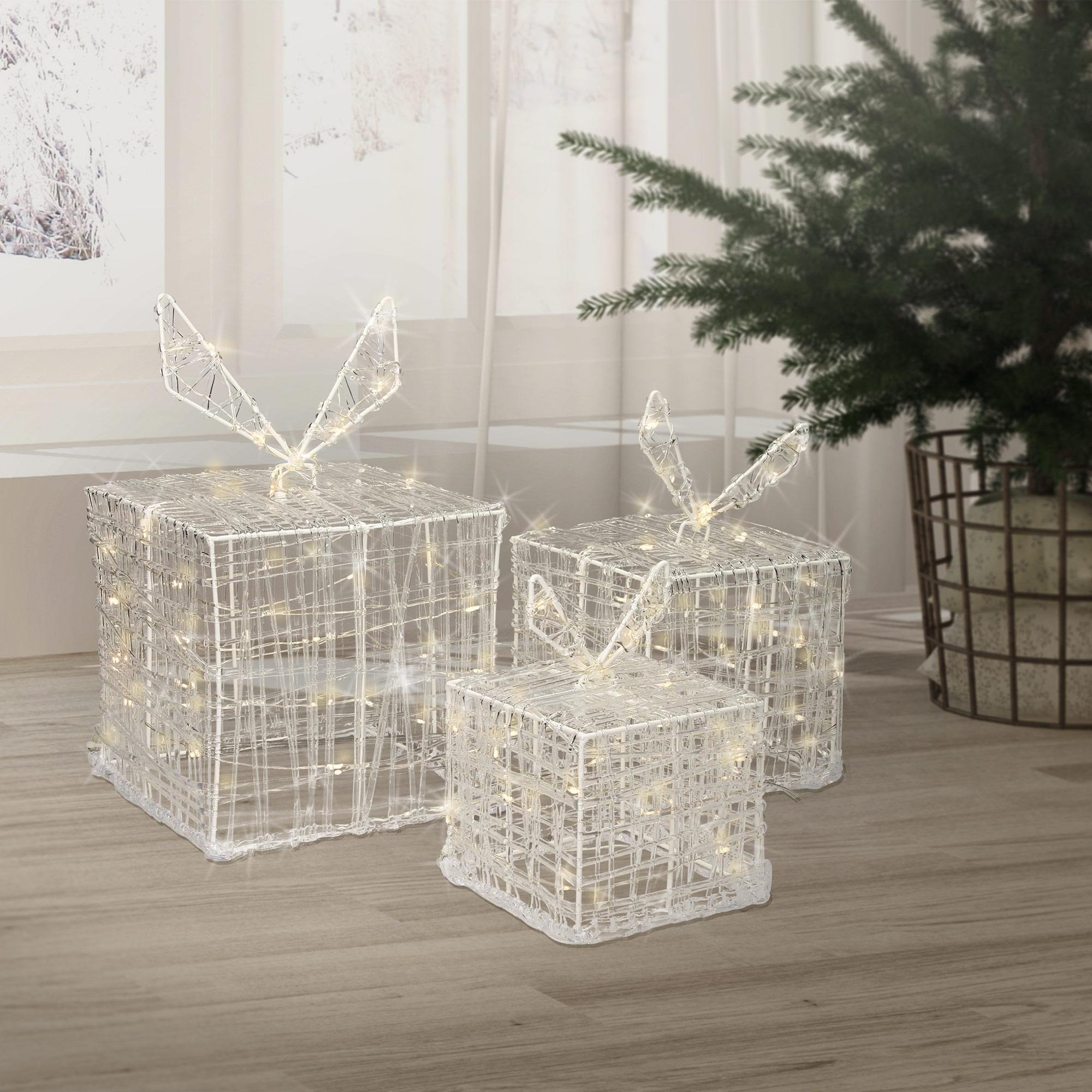Drei beleuchtete Geschenkboxen mit Schleifen stehen auf einem Holzboden, in der Nähe eines Weihnachtsbaums und eines Fensters.