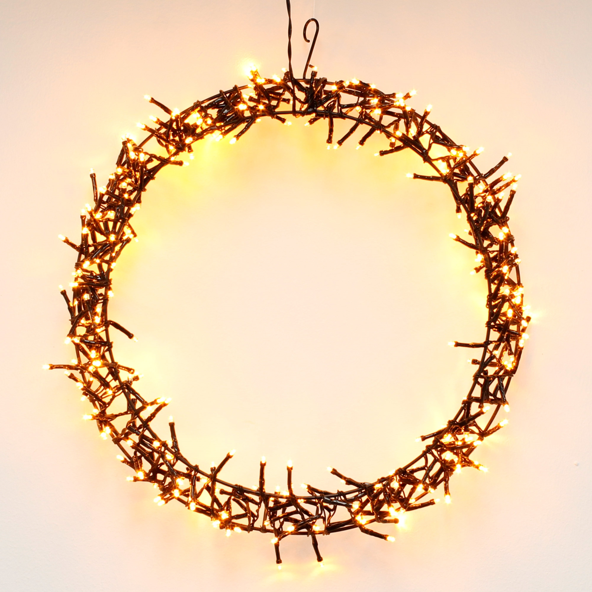 Ein kreisförmiger Weihnachtslichtkranz mit warmweißen Lichtern, vor weißem Hintergrund hängend.