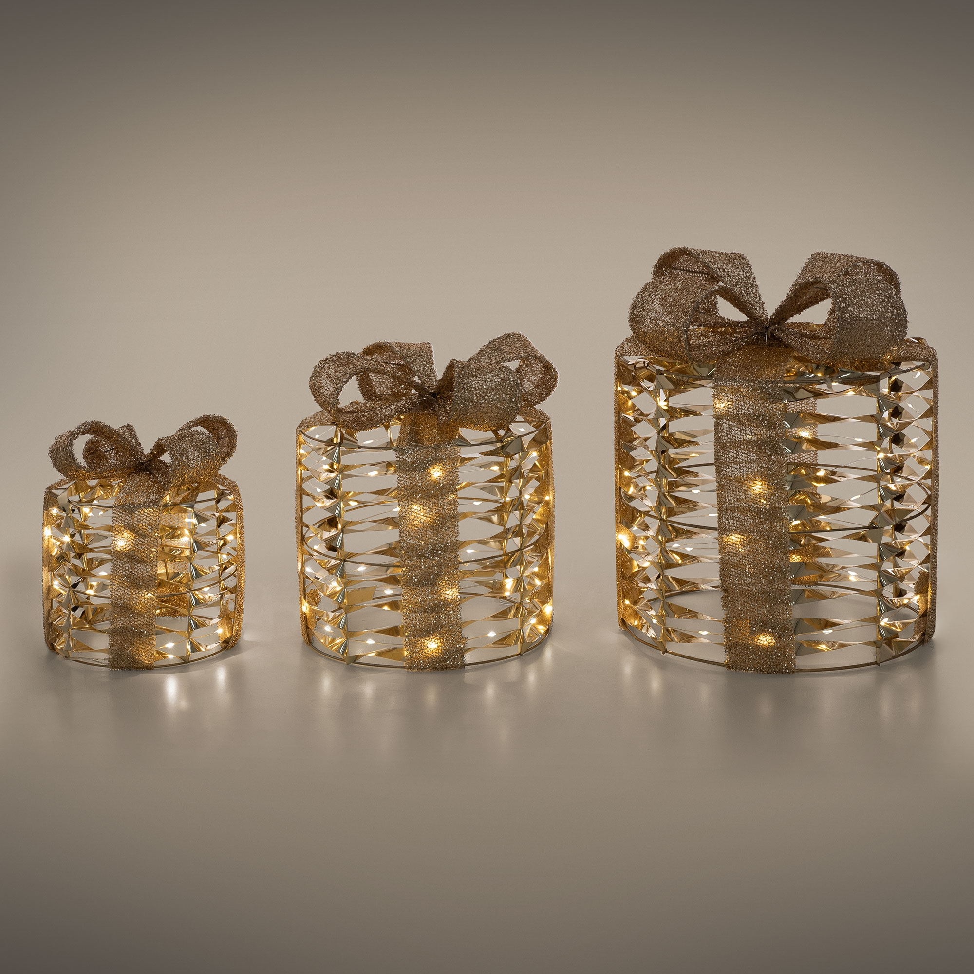 Drei beleuchtete Geschenkboxen mit goldenen Schleifen. Sie haben ein metallisches Design mit Lichtern im Inneren und stehen auf einer hellen Oberfläche.