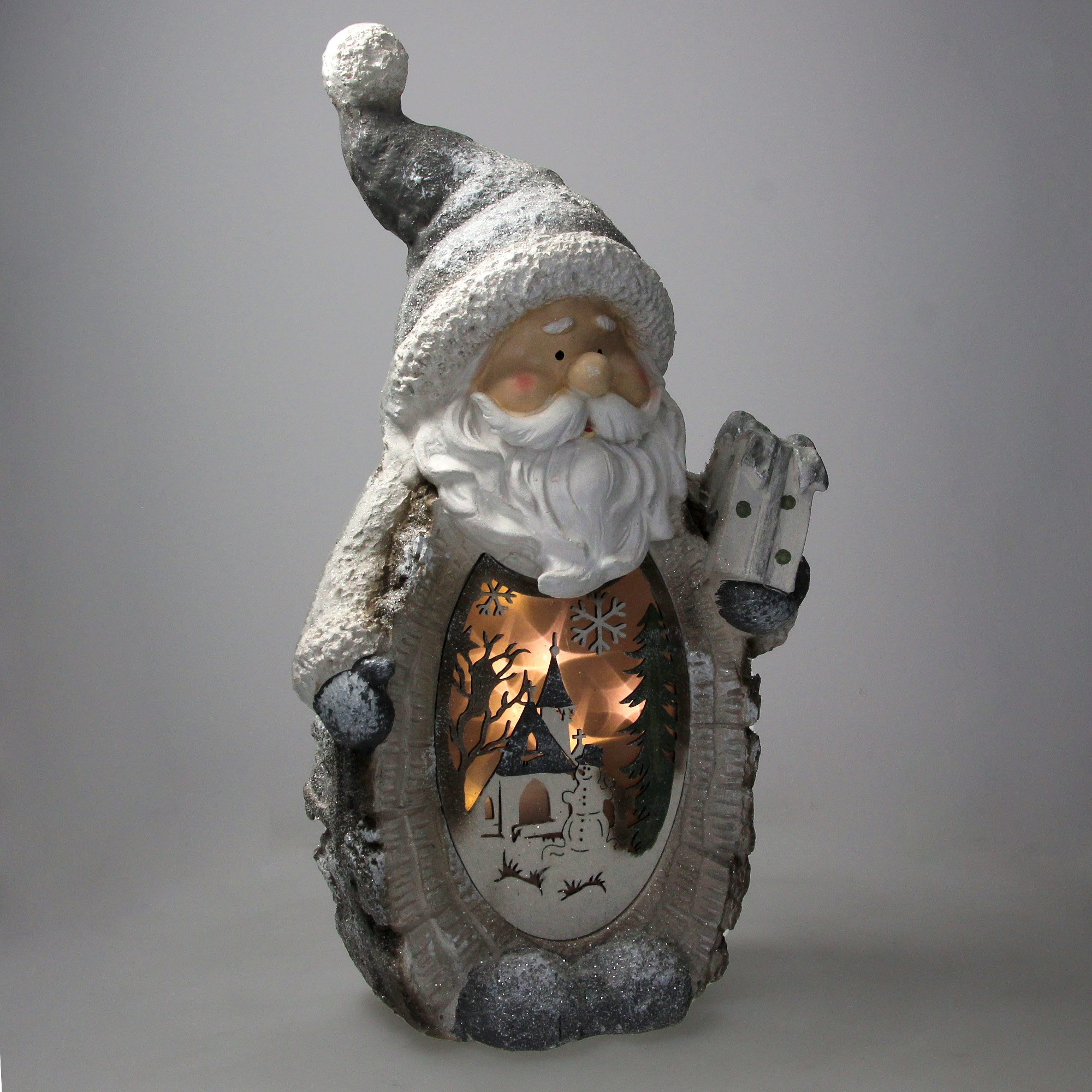 Weihnachtsmann-Figur mit einer Winterszene im Inneren. Mit Kirche, Schneemann und Bäumen. Die Figur ist grau und weiß.
