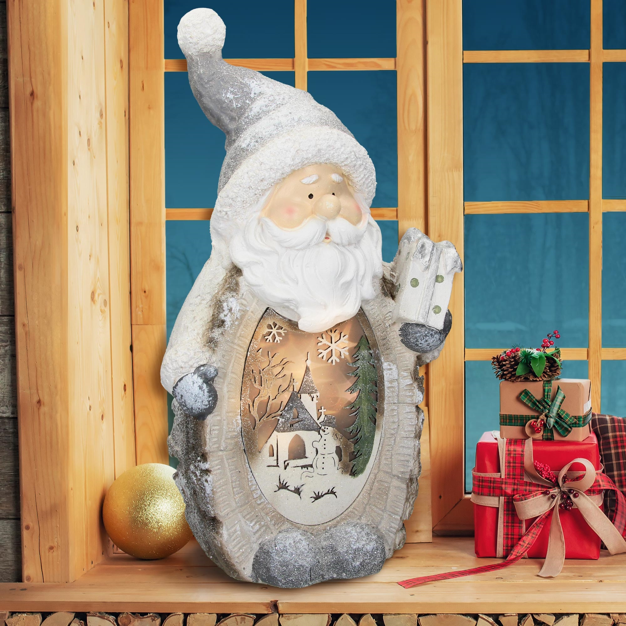 Weihnachtsmannfigur mit Winterszene. Geschenke und Dekorationen auf Holz vor Fenster.