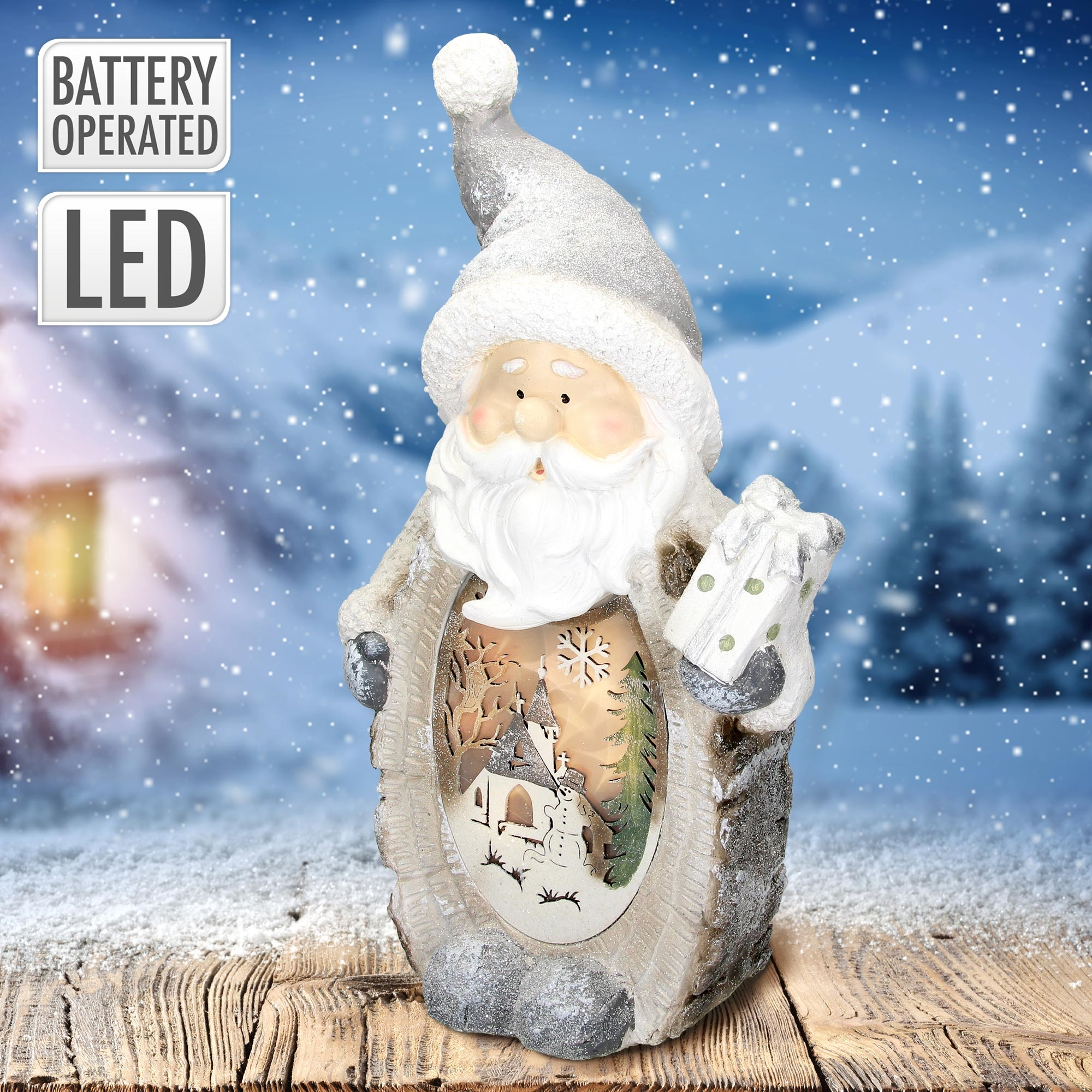 Weihnachtsmann-Figur mit Winterszene im Inneren. Hält ein Geschenk. Schnee fällt im Hintergrund. Holztisch davor.
