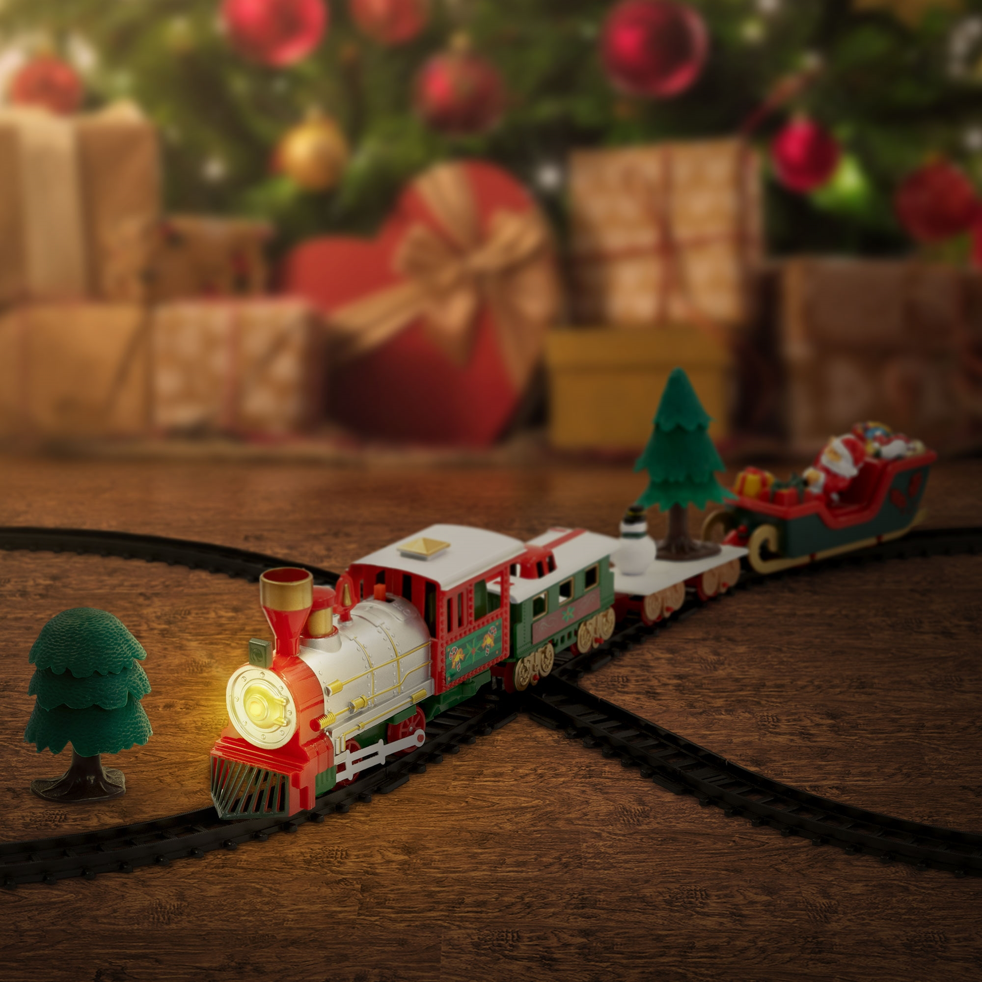Ein Spielzeug-Weihnachtszug auf Gleisen. Der Zug ist rot, grün und weiß. Im Hintergrund ein Weihnachtsbaum und Geschenke.