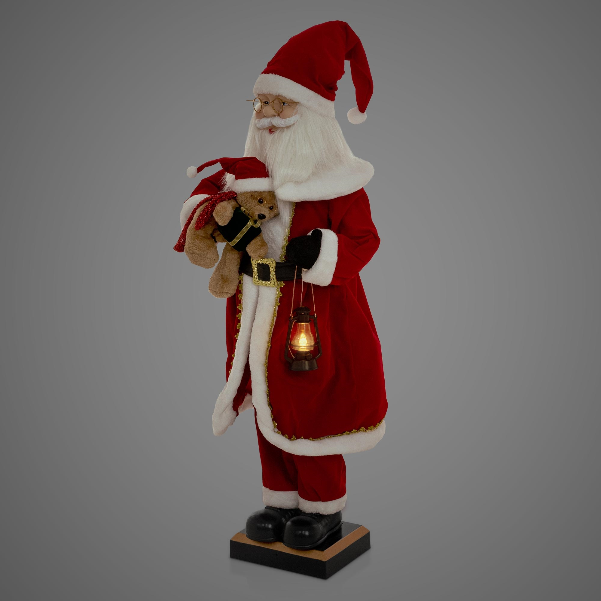 Weihnachtsmann-Figur, roter Anzug, weißer Bart, hält Teddybär und Laterne. Grauer Hintergrund, schwarze Schuhe und Sockel.