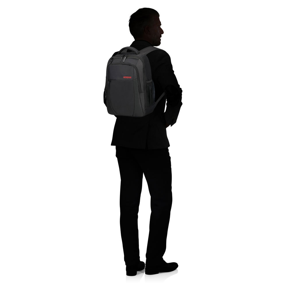 Ein Mann im schwarzen Anzug steht mit dem Rücken zum Betrachter und trägt einen schwarzen Rucksack. Der Hintergrund ist weiß.