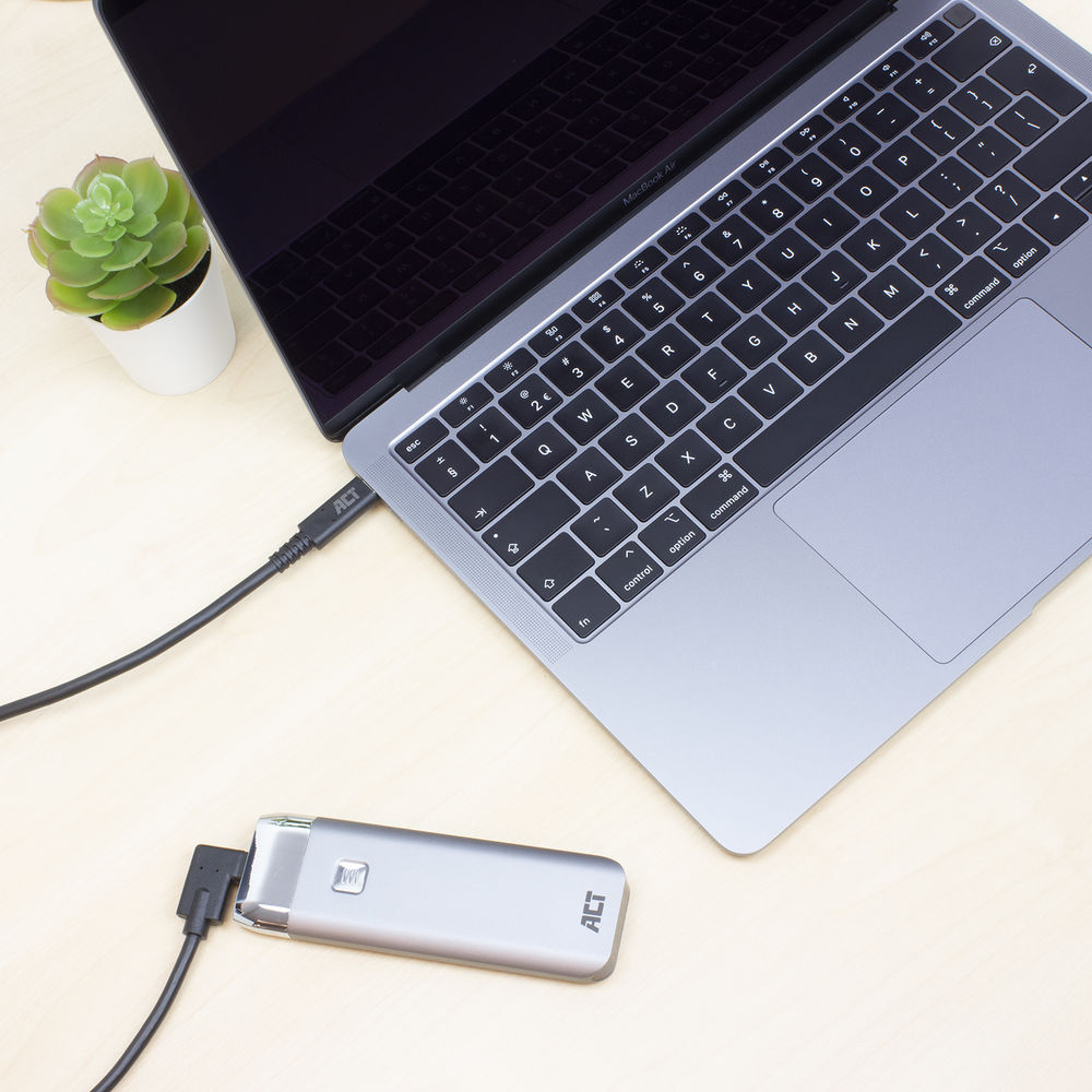 Laptop met een aangesloten zilverkleurig apparaat en een kleine plant. De laptop is open, de toetsenbord is zichtbaar. Een kabel verbindt het apparaat.