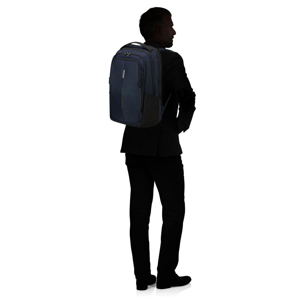 Ein Mann in einem schwarzen Anzug mit einem blauen Rucksack steht vor einem weißen Hintergrund, von hinten gesehen. Die Silhouette ist sichtbar.