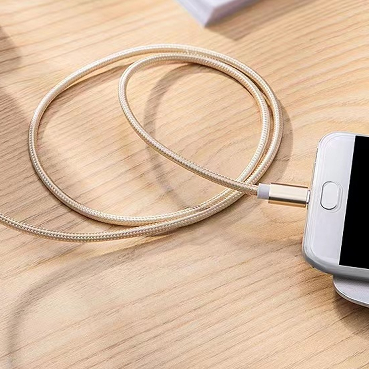 Ein goldfarbenes Ladekabel ist mit einem weißen Smartphone auf einer Holzoberfläche verbunden. Das Kabel ist aufgerollt.