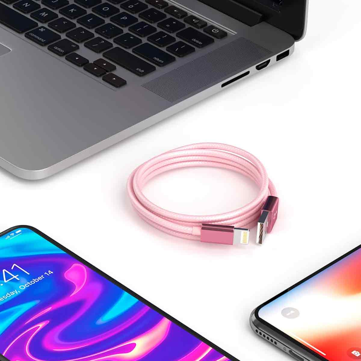 Ein Laptop, zwei Smartphones und ein pinkfarbenes Ladekabel liegen auf einer weißen Oberfläche. Die Telefone und das Kabel sind im Vordergrund.