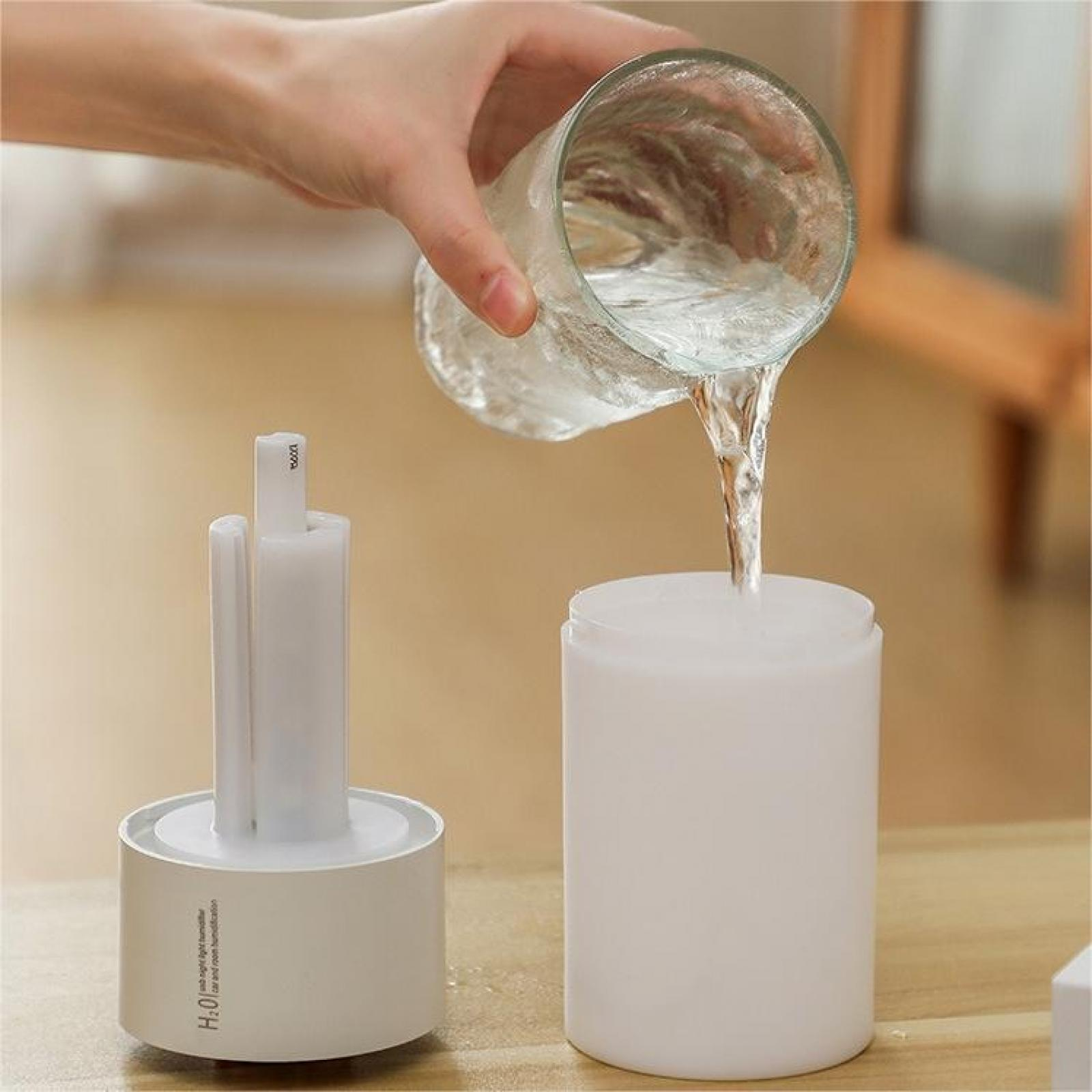 Eine Hand gießt Wasser aus einem Glas in einen weißen Luftbefeuchter. Links ist ein weißer Luftbefeuchter.