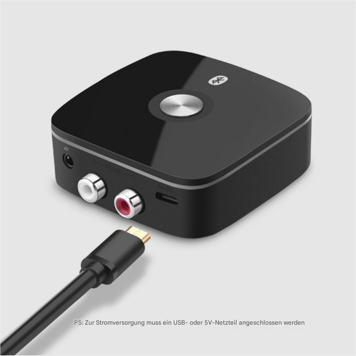 Ein schwarzer Bluetooth-Audioempfänger mit Audioanschlüssen und einem angeschlossenen USB-Kabel. Ein silberner Knopf und ein Bluetooth-Symbol sind sichtbar.