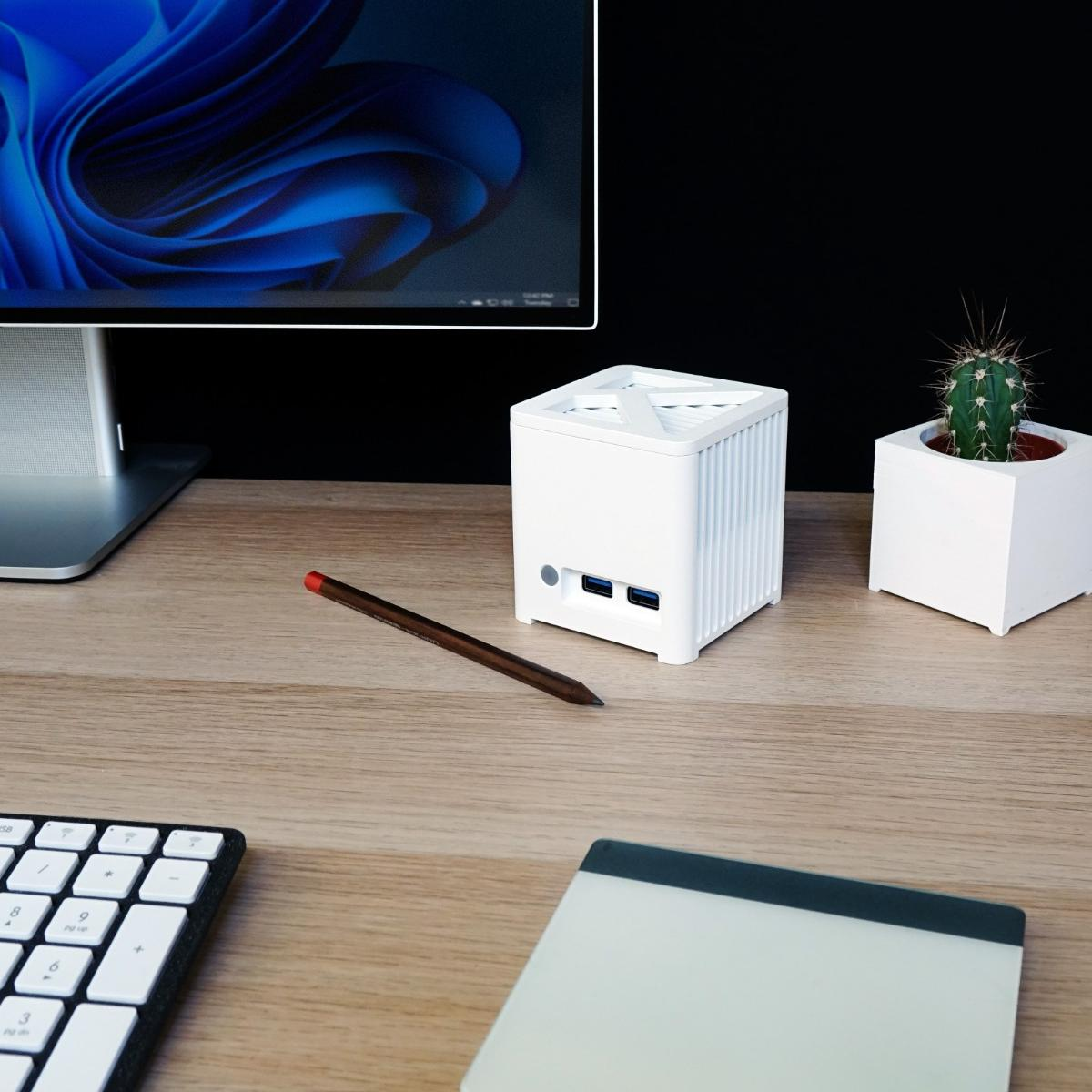 Biurko z komputerem, białym mini PC, kaktusem, ołówkiem, klawiaturą i notatnikiem.