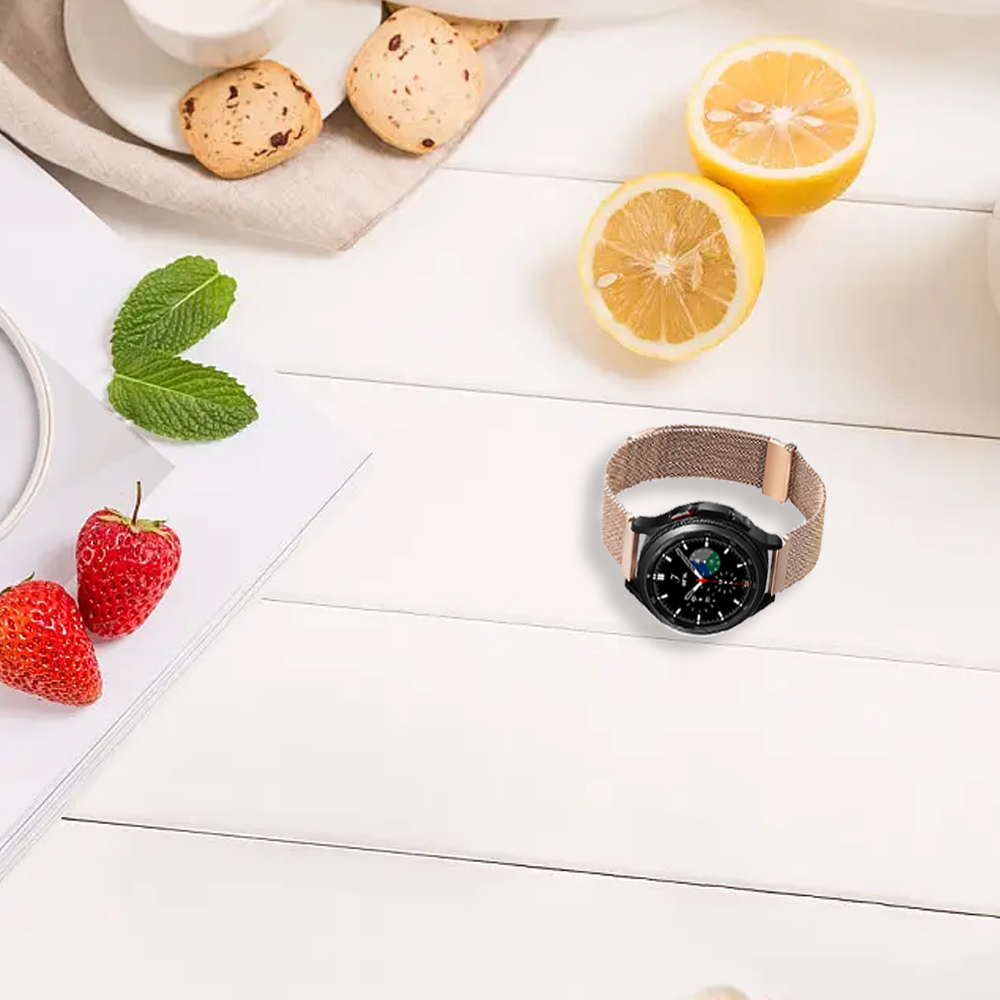 Eine Uhr mit beigem Armband liegt auf einer weißen Holzoberfläche. Erdbeeren, Zitronenhälften, Kekse und Minzblätter sind vorhanden.