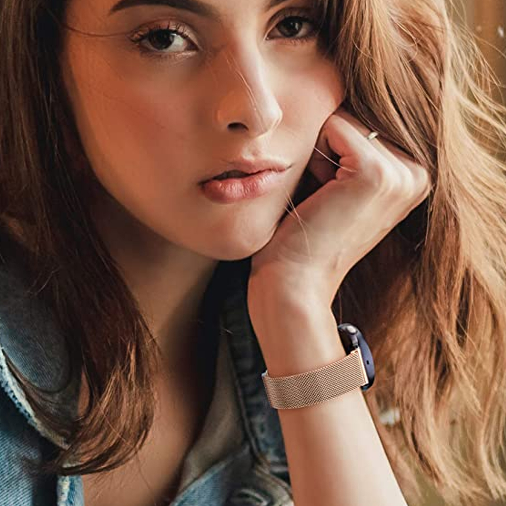 Eine Frau mit braunem Haar stützt ihr Gesicht auf ihre Hand, mit einer Uhr mit goldenem Mesh-Armband.