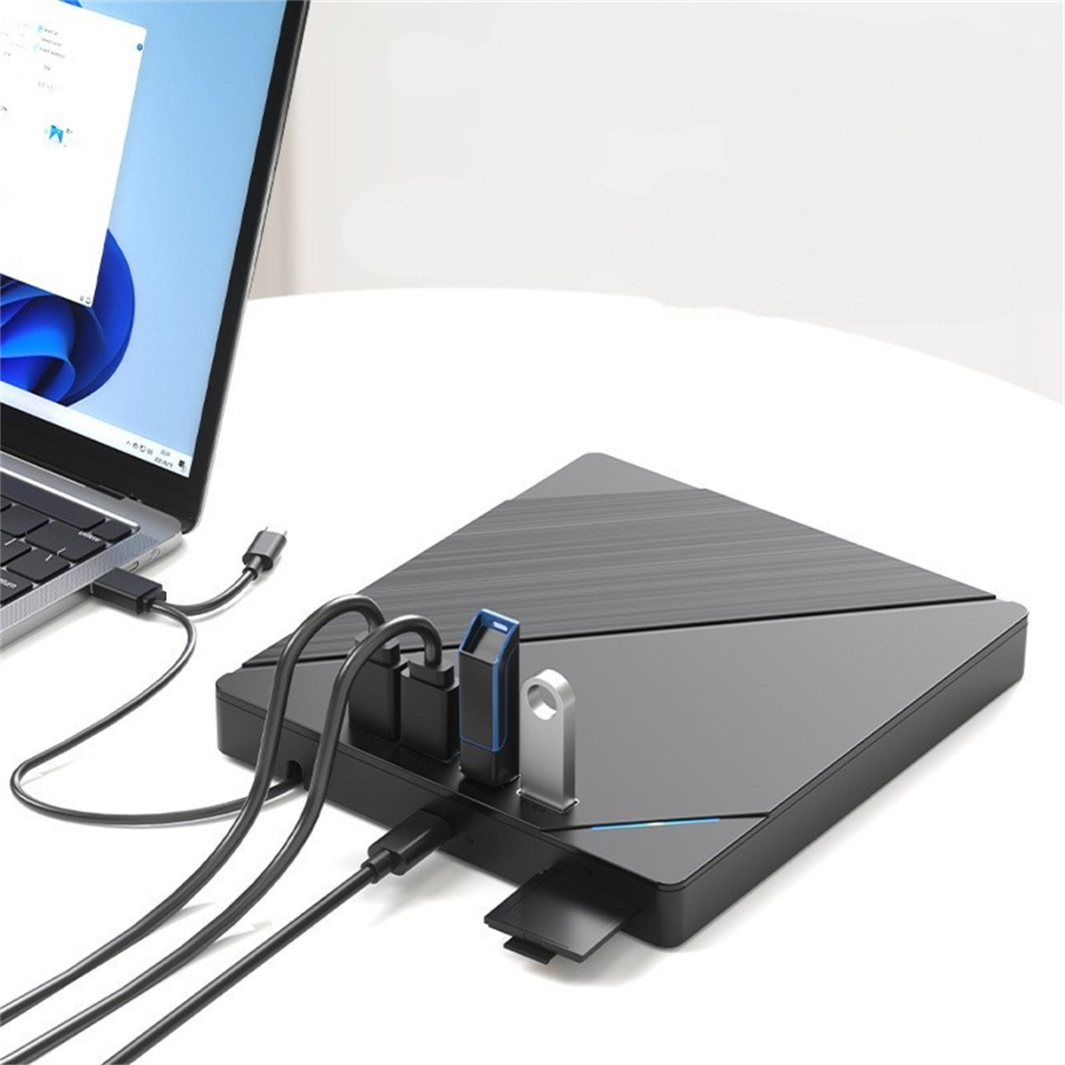 Ein Laptop ist mit einem schwarzen USB-Hub verbunden, auf dem USB-Laufwerke und Kabel liegen, auf weißer Oberfläche. Der Hintergrund ist weiß.