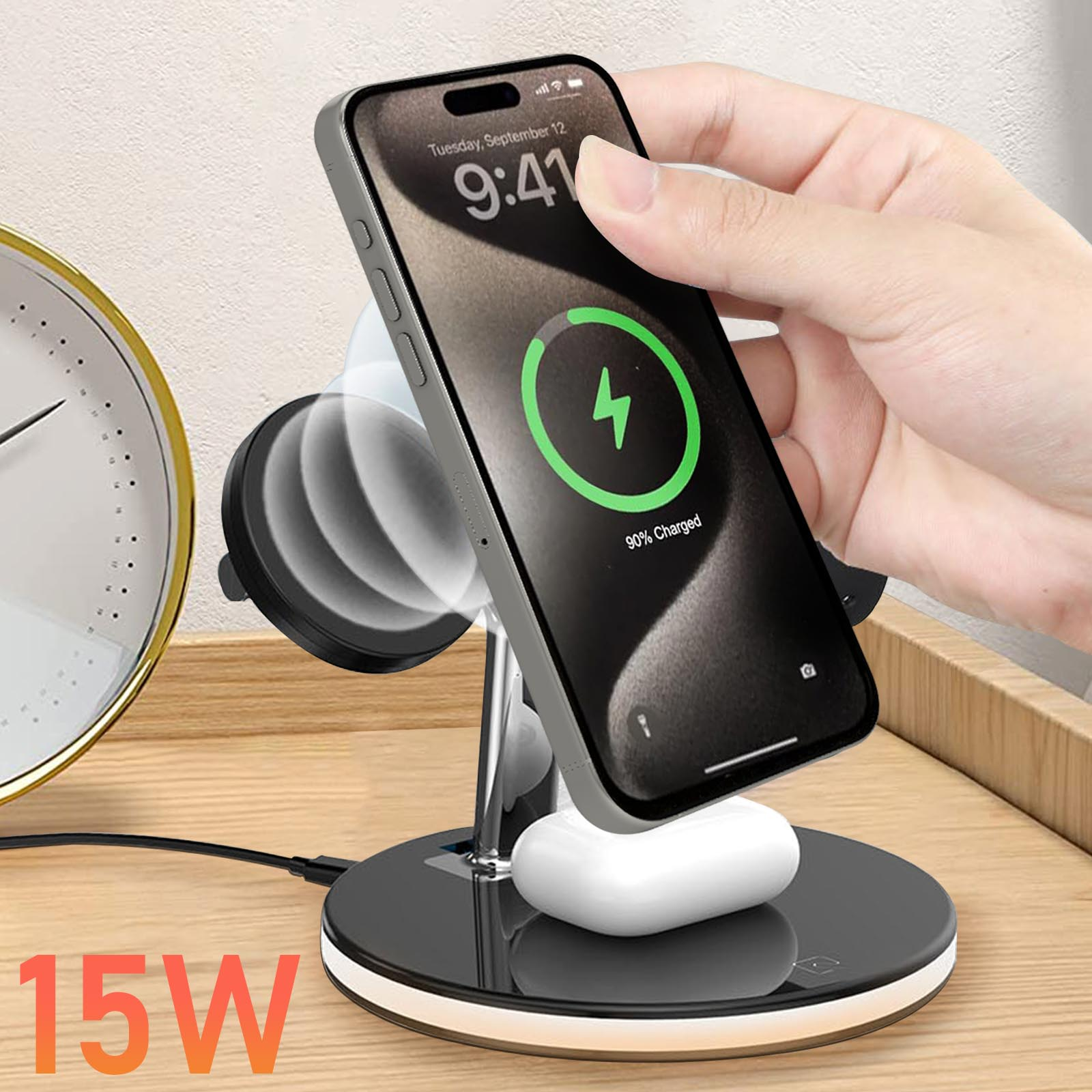 Eine Hand hält ein ladendes iPhone, das 9:41 und 90 % geladen anzeigt. Ein Ladeständer mit AirPods und eine Uhr sind ebenfalls sichtbar.
