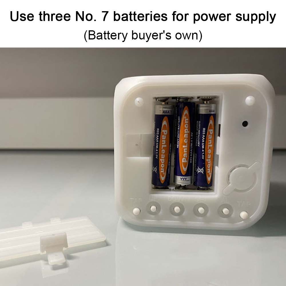 Offene weiße Uhr mit drei Batterien. Batteriefach offen, AAAs sichtbar. Der Hintergrund ist eine helle Oberfläche.