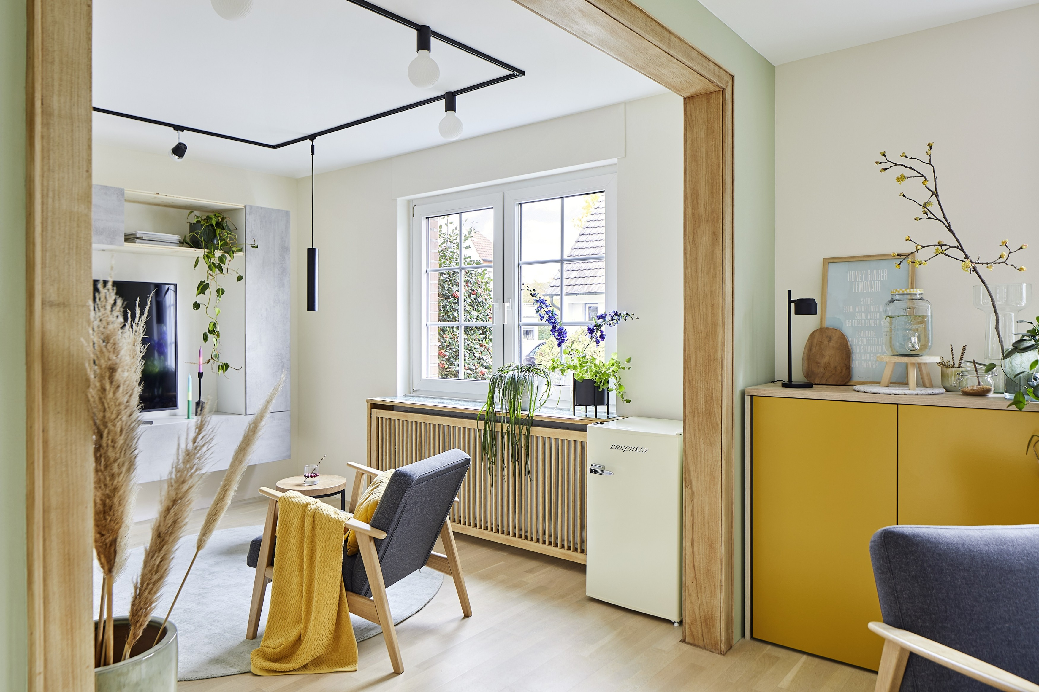 Wohnzimmer mit Pflanzen, Fenster, grauem Stuhl, gelber Decke und Schrank. Neutrale Töne mit Holzakzenten.