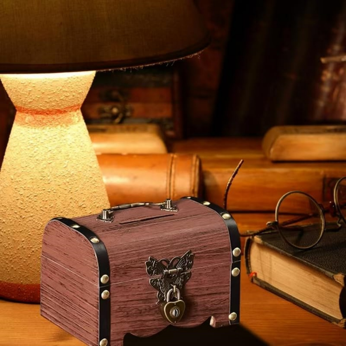 Eine hölzerne Schatzkiste mit Schloss steht auf einem Schreibtisch neben einer Lampe und Büchern. Rechts steht eine Brille.