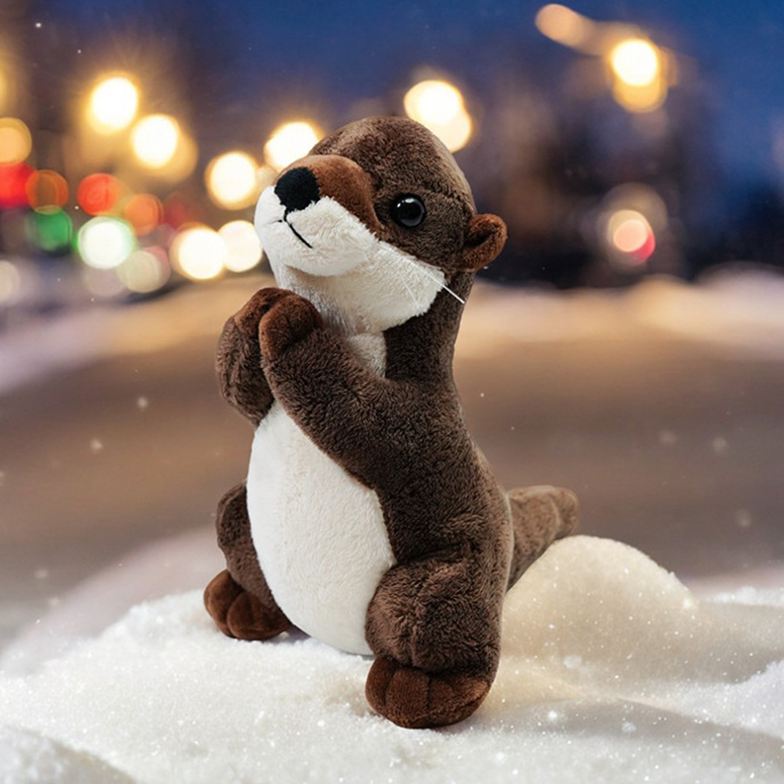 Ein Stoffotter mit braunem Fell und weißem Bauch sitzt im Schnee. Er befindet sich in einer Gebetshaltung, mit Bokeh-Lichtern im Hintergrund.