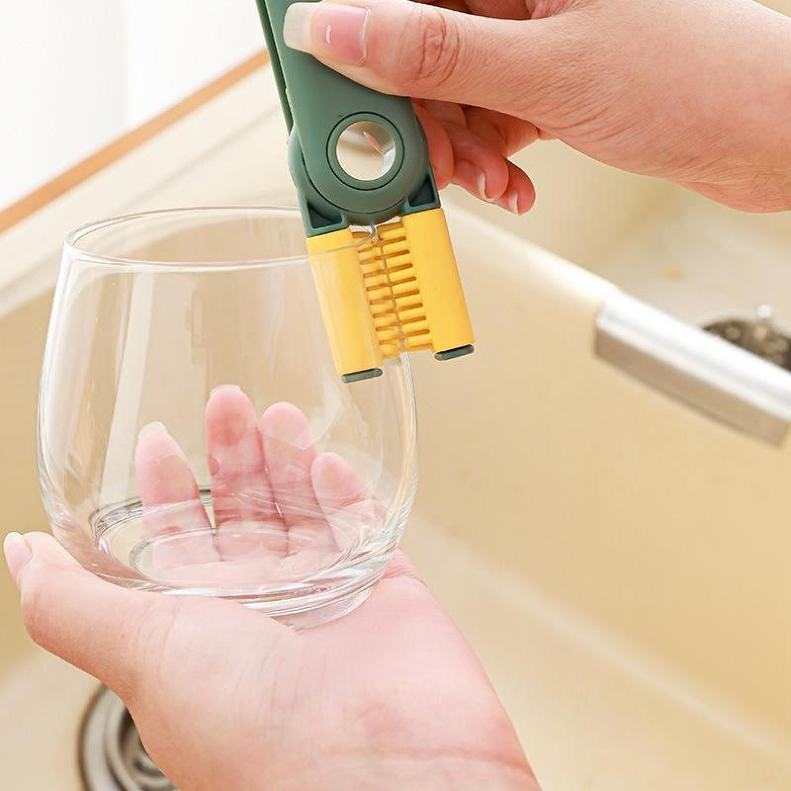 Eine Person hält einen grünen und gelben Glasreiniger über einem klaren Glas. Im Hintergrund ist ein Waschbecken.