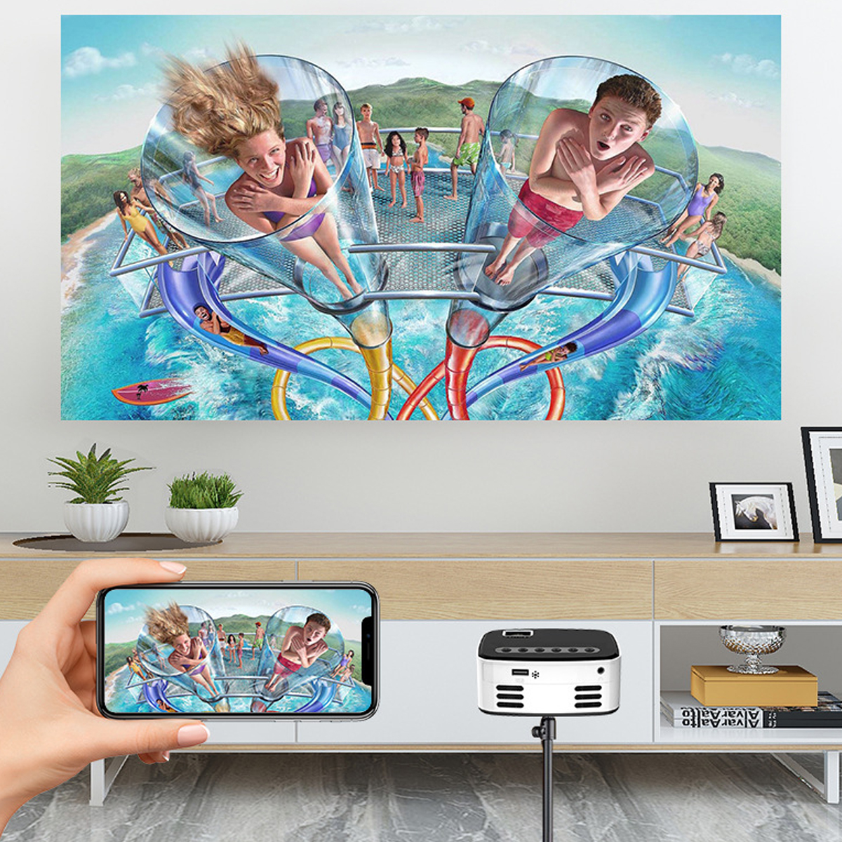 Ein Projektor zeigt ein Wasserparkbild. Ein Telefon zeigt dasselbe Bild. Eine Person hält das Telefon. Ein Gerät befindet sich vor dem Telefon.