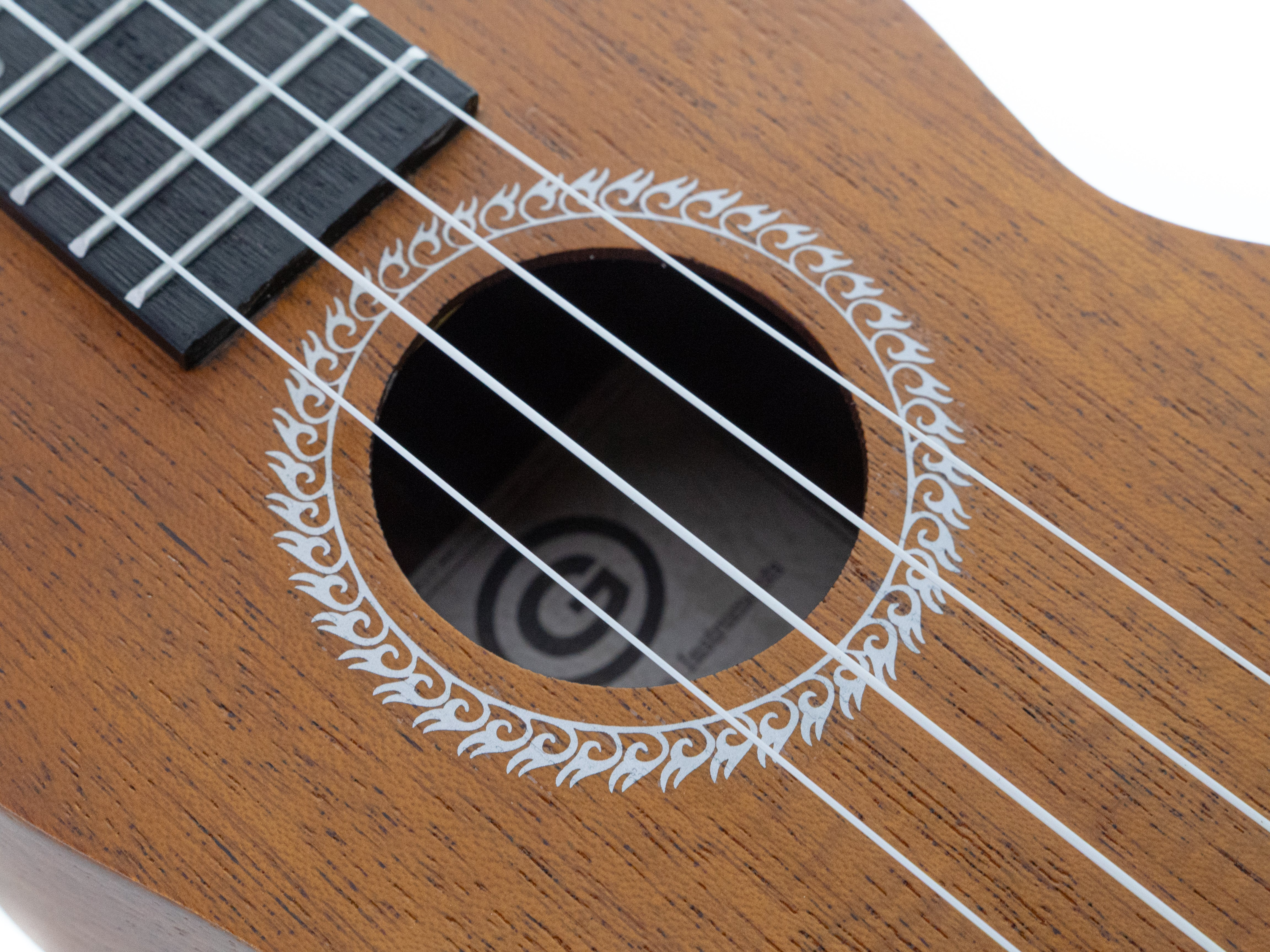 Nahaufnahme einer Ukulele. Brauner Holzkörper mit Schallloch, weiße Saiten und Griffbrett. Weiße Zierleiste.