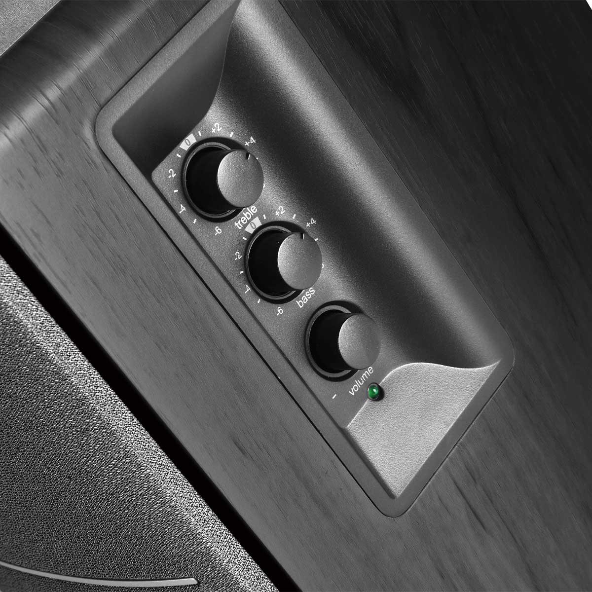 Zbliżenie panelu sterowania głośnikiem. Posiada pokrętła tonów wysokich, basów i głośności z zielonym światłem zasilania.