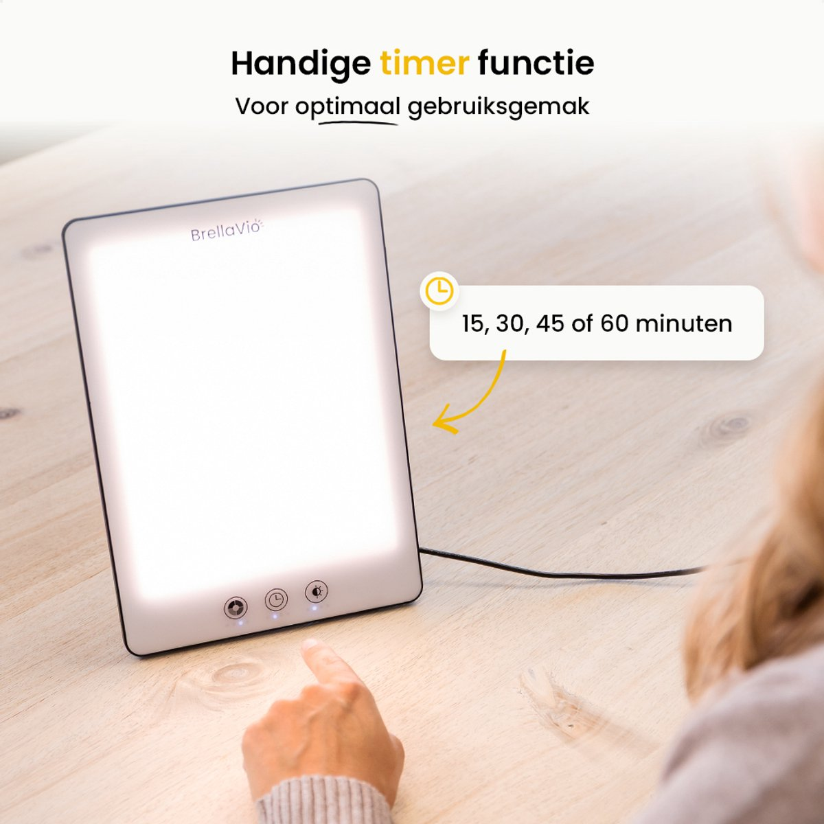 A white light therapy lamp with timer options (15, 30, 45, or 60 minutes) on a wooden table. A person's hand points to the lamp.