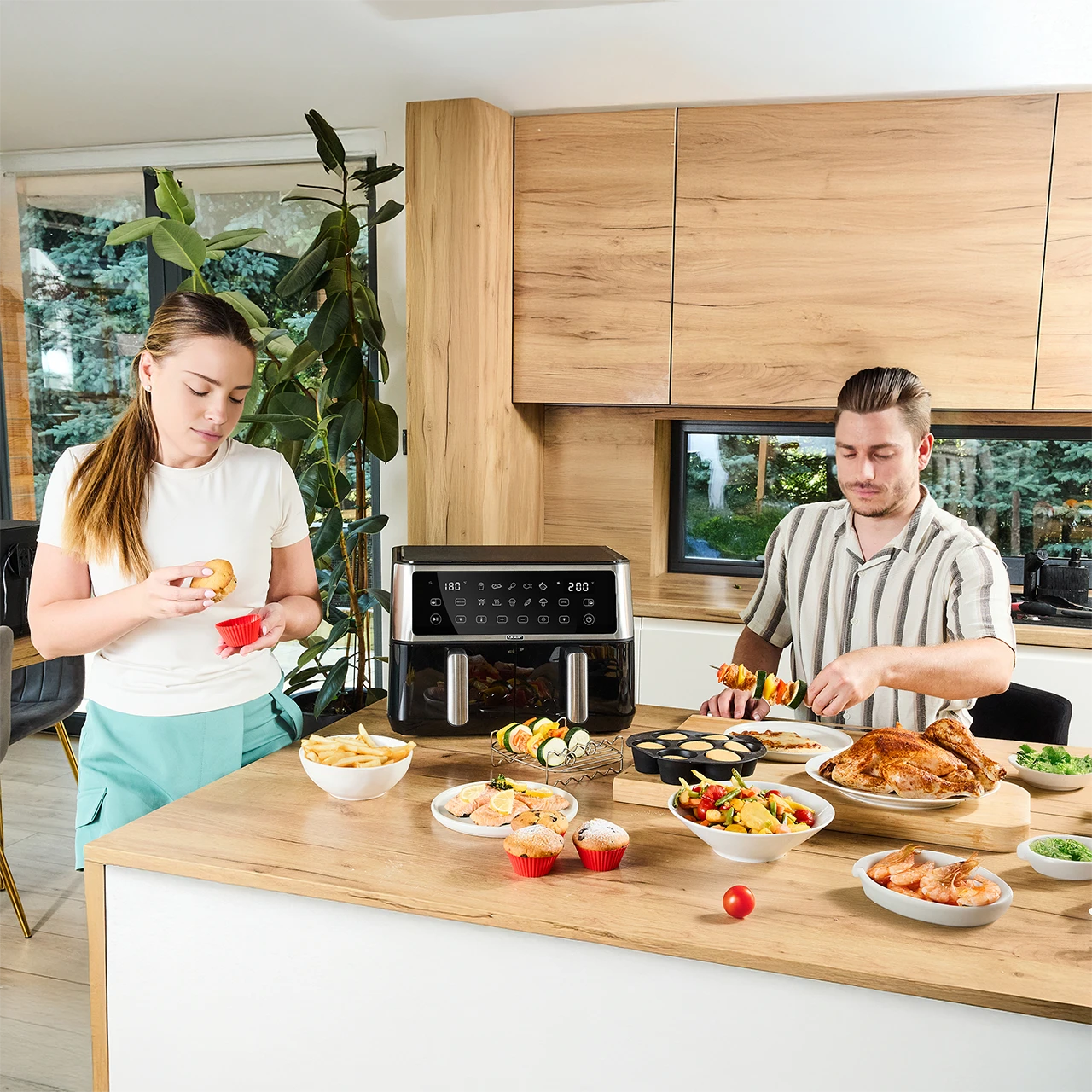Para przygotowuje jedzenie w kuchni. Na blacie stoi frytkownica powietrzna, różne potrawy i cały pieczony kurczak.