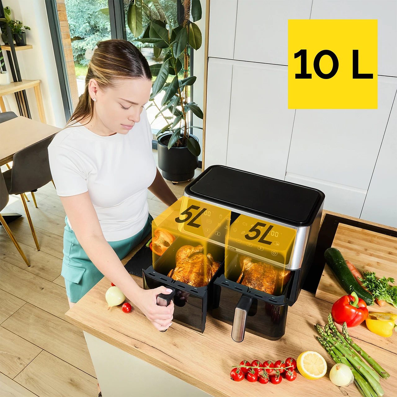 Kobieta używa frytkownicy beztłuszczowej z podwójnym koszem. Ma dwie komory 5L, każda z pieczonym kurczakiem. Warzywa i owoce na blacie.