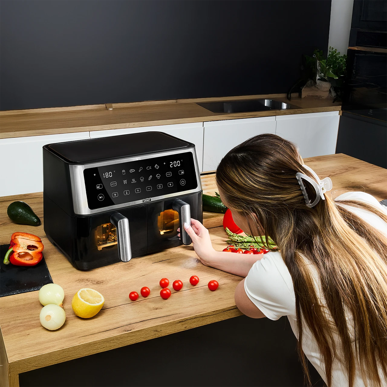 Kobieta przygotowuje jedzenie z frytownicą powietrzną. Warzywa takie jak pomidory, cebula i awokado leżą na drewnianej powierzchni.