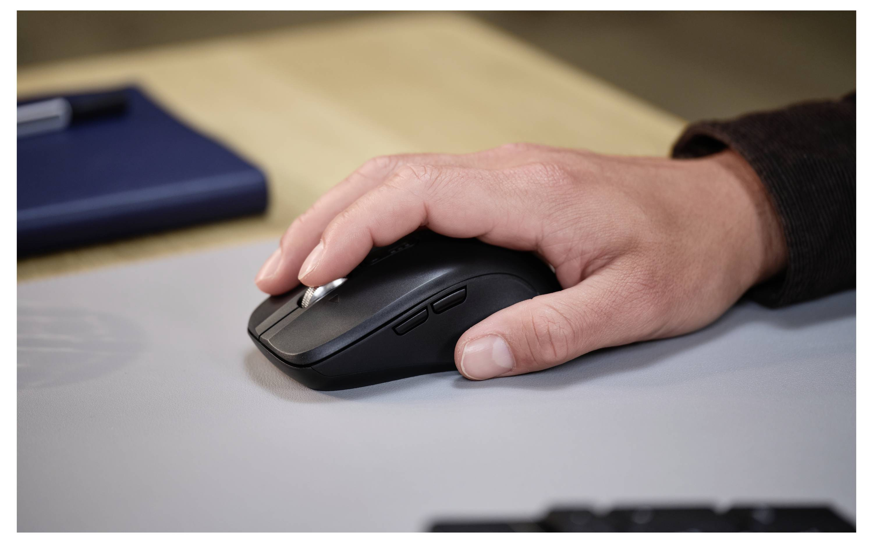 Een hand rust op een zwarte computermuis. Een blauw object staat op de achtergrond op een licht oppervlak.