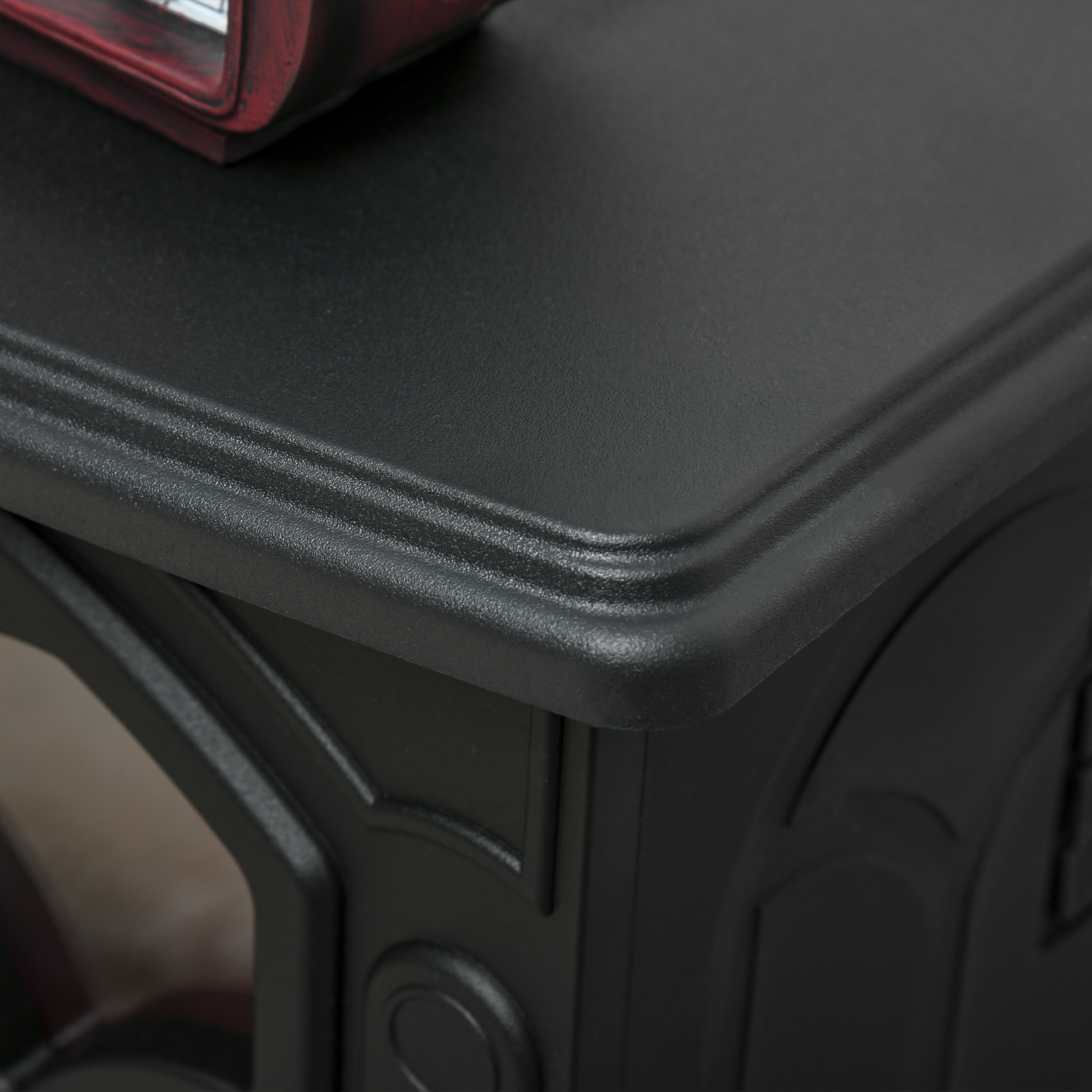 Primer plano de una esquina de mesa negra con borde decorativo. Un objeto rojo parcialmente visible en la parte superior.