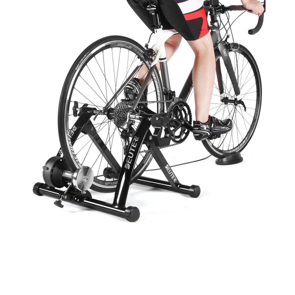 Ciclista en un rodillo estático. Bicicleta negra con pantalones cortos rojos y negros. Fondo blanco.