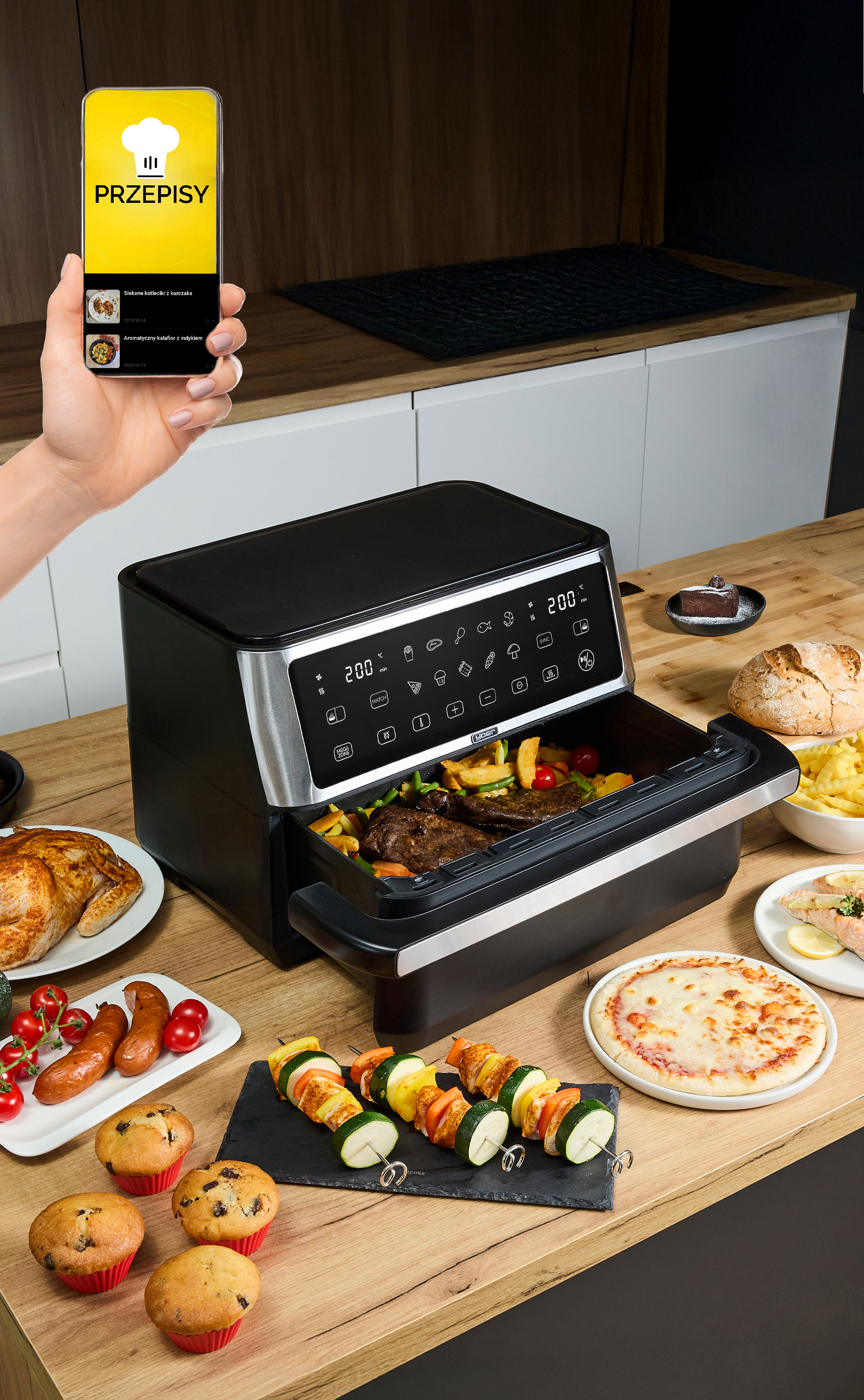 Frytownica powietrzna z jedzeniem, telefon z przepisami i różne dania na drewnianym stole.