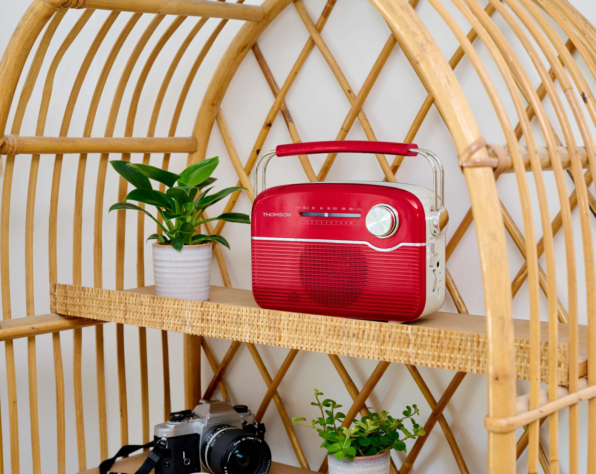 Czerwone radio Thomson stoi na półce z roślinami i aparatem na bambusowej półce.