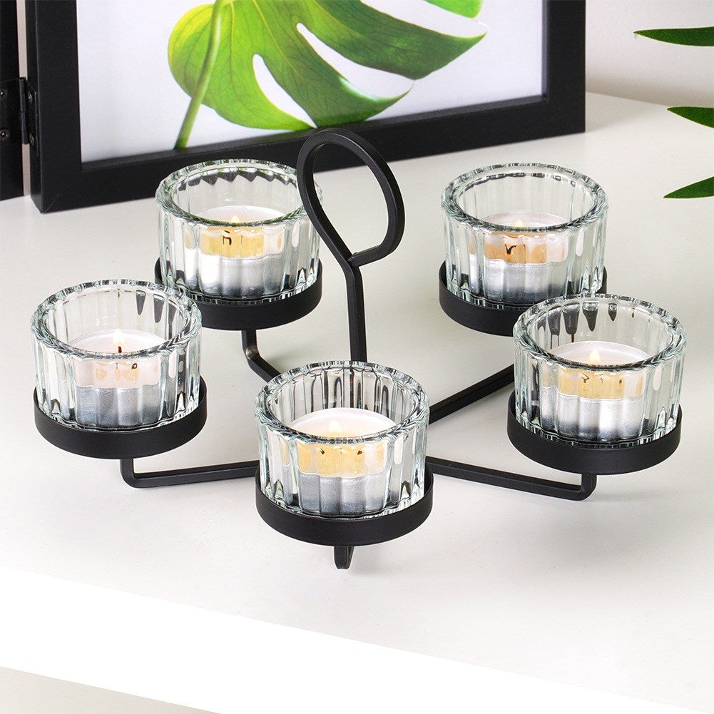 Un portavelas de metal negro con cinco candelabros de vidrio, cada uno con una vela encendida, sobre una superficie blanca.